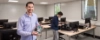Ein Mann hält ein Computerteil in einem Klassenzimmer mit mehreren Computern und einem anderen Mann im Hintergrund.