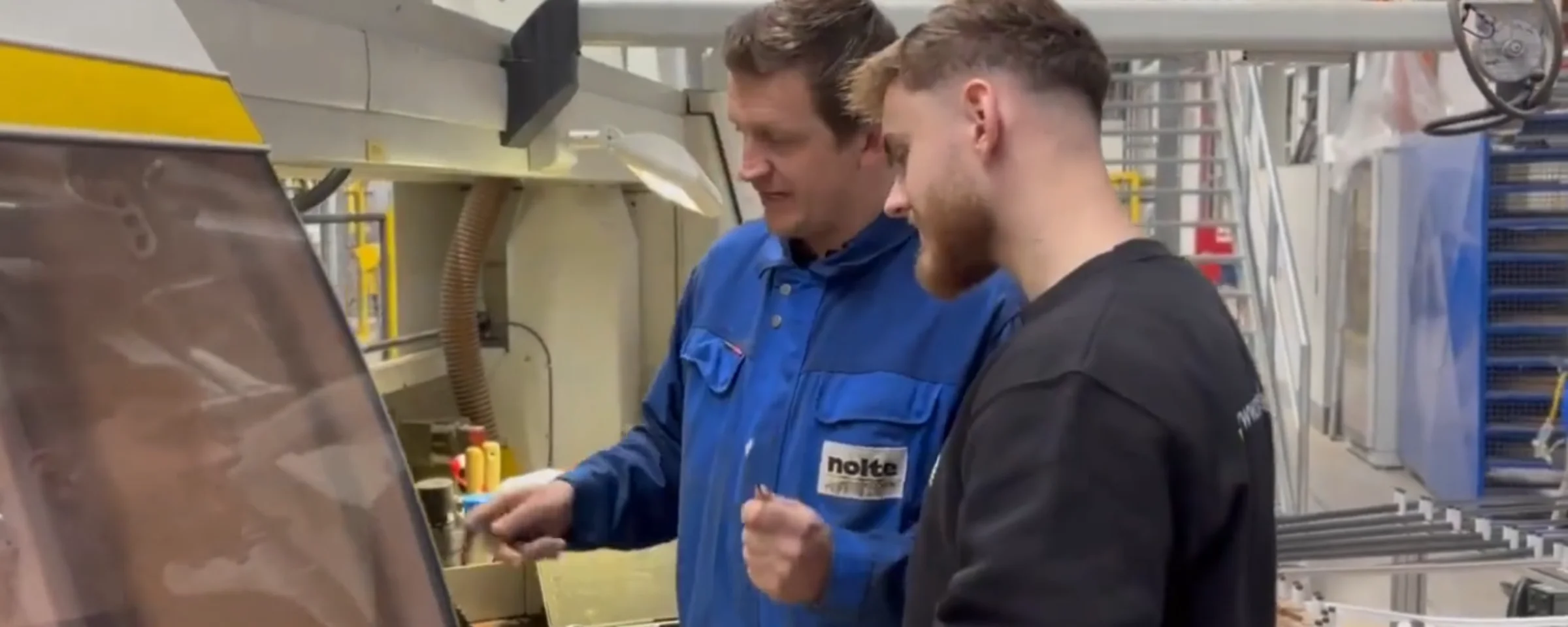 Zwei Männer arbeiten in einer Fabrik an einer Maschine, Nolte Küchen.