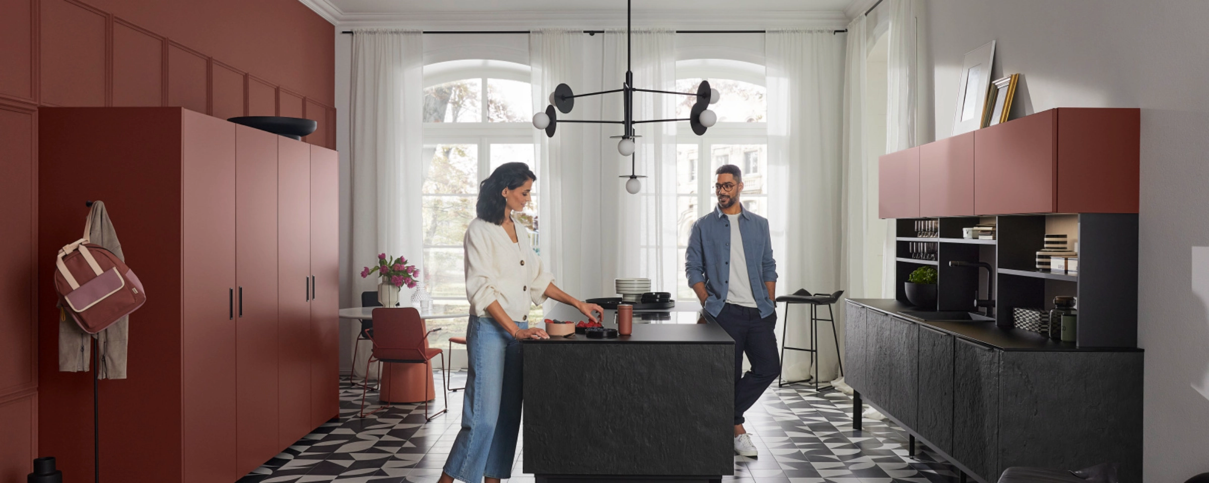 Une cuisine moderne de Nolte Kitchen avec deux personnes, sol en carreaux géométriques et armoires rouges.