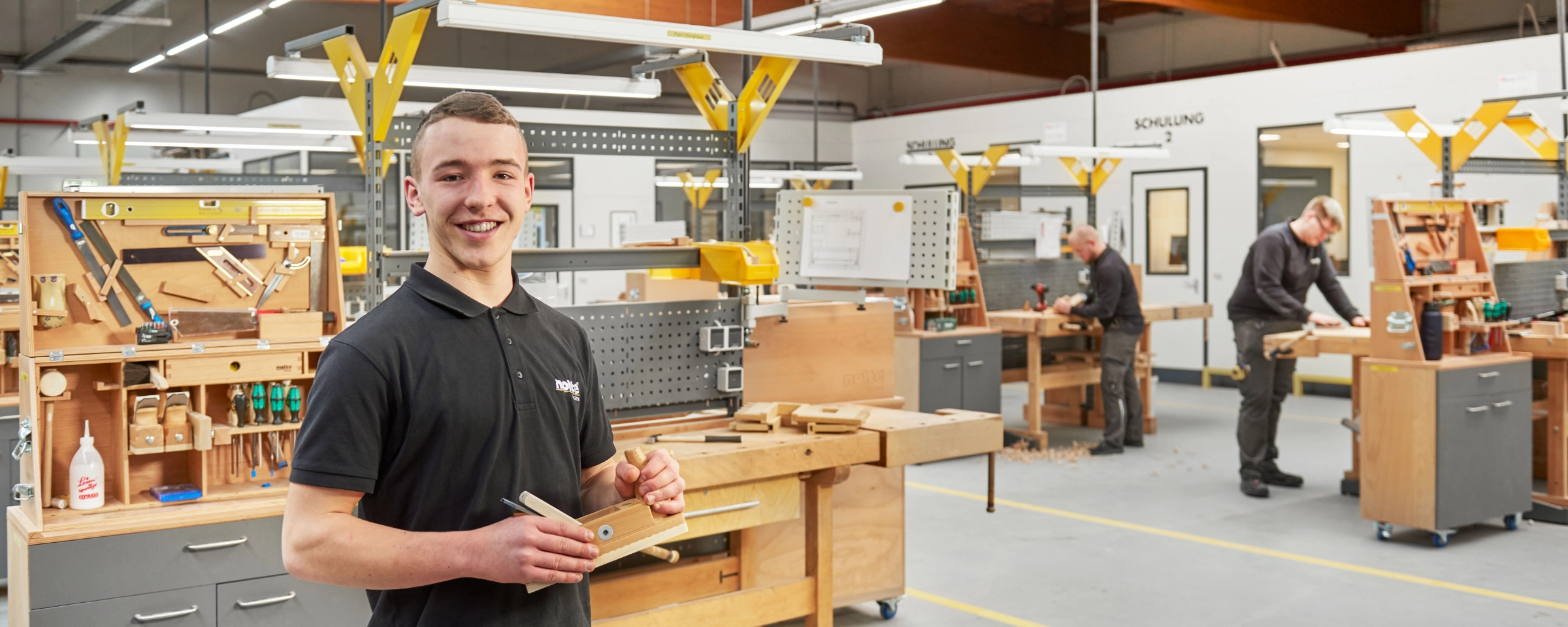 Ein junger Mann in einer Werkstatt mit mehreren Arbeitstischen und Werkzeugen.