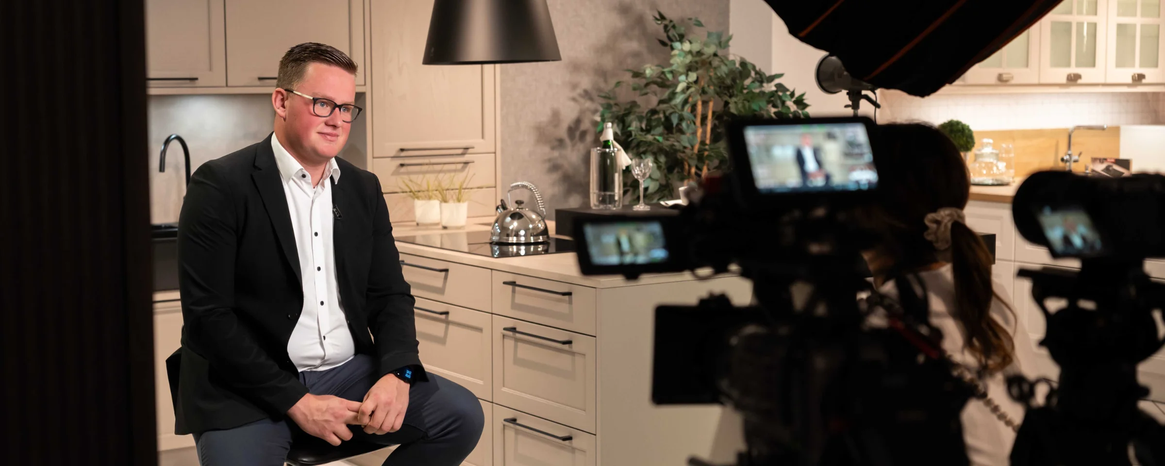 A man sits in a modern Nolte kitchen in front of cameras.