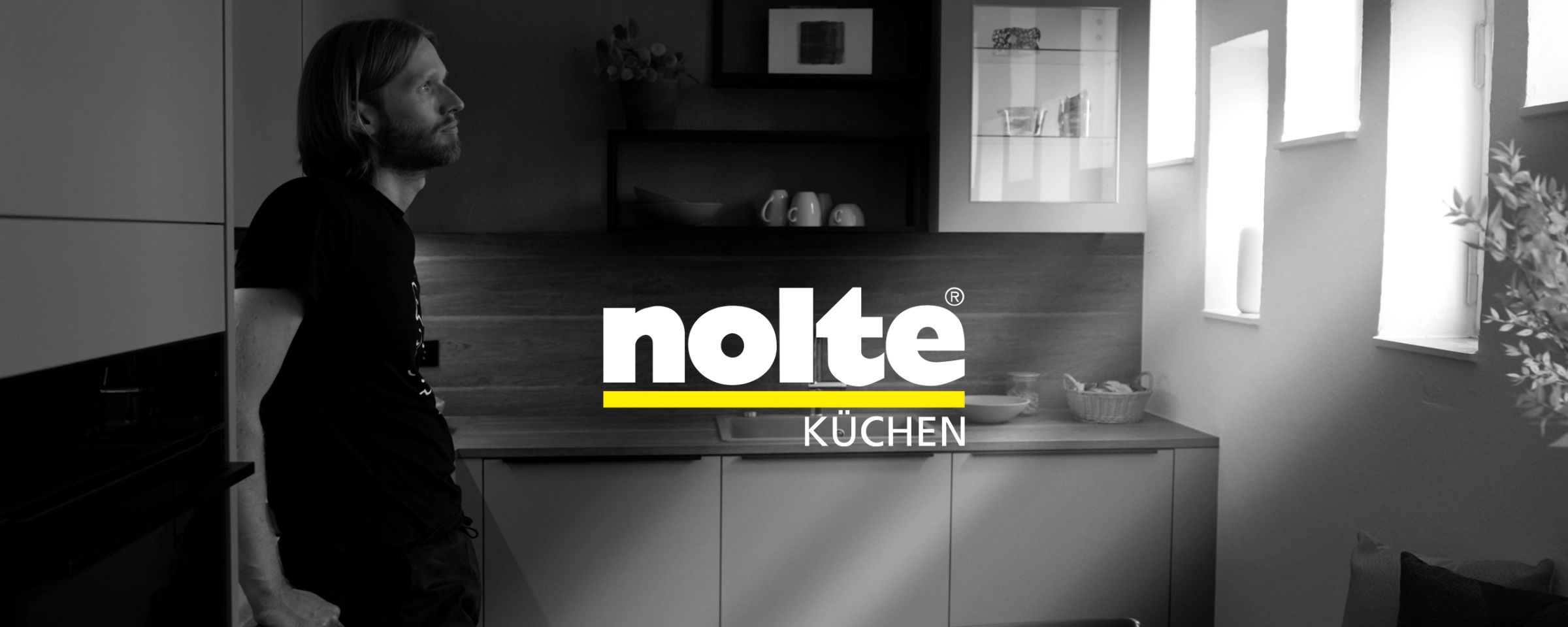 Ein Mann lehnt an der Arbeitsplatte in einer modernen Küche von Nolte Küchen.