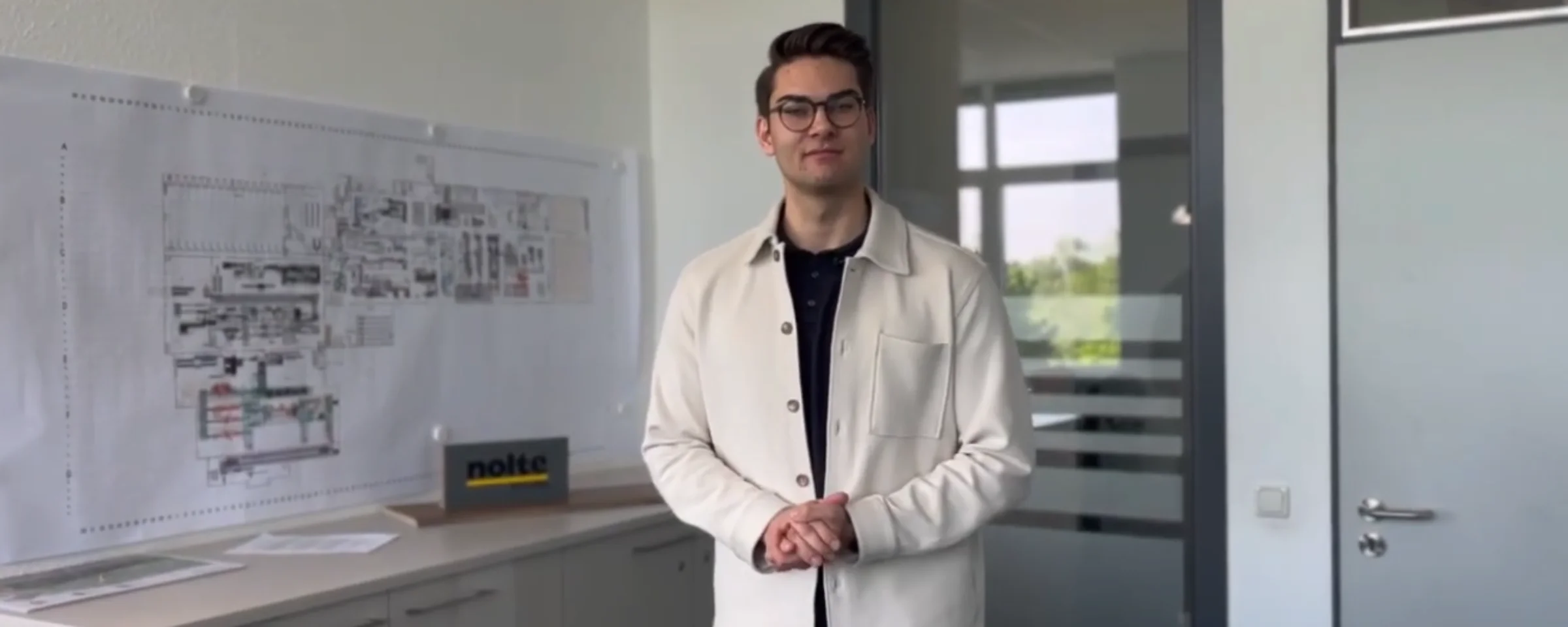 Ein Mann steht in einem Büro neben Bauplänen und einem Nolte Küchen-Schild.