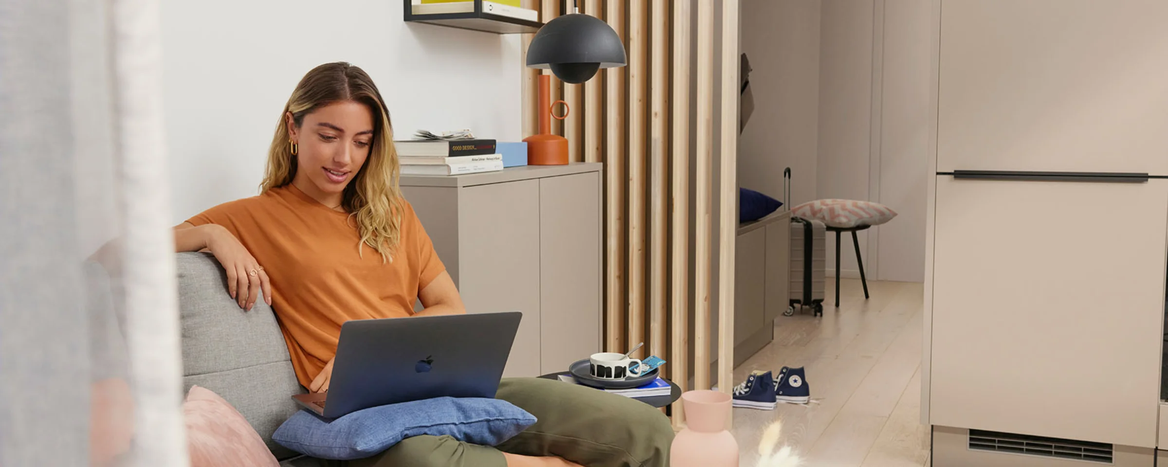 Eine Frau sitzt in einem modernen Wohnzimmer auf einem Sofa mit einem Laptop, umgeben von stilvollen Dekorationen von Nolte Living.