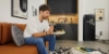 A man eating on a sofa in a room with Nolte kitchen cabinets.
