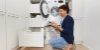 Un homme agenouillé dans une buanderie charge du linge dans une machine à laver. Nolte buanderies.