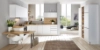 Cuisine Nolte claire avec le programme de façades PLUS en blanc softmatt, combinée avec des plans de travail en bois et un espace de travail intégré dans un environnement de vie ouvert et baigné de lumière.