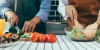Deux personnes préparent ensemble un repas. Sur un plan de travail de cuisine, des légumes sont coupés et une salade est mélangée.