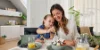 Młoda kobieta w nowoczesnym, kompaktowym aneksie kuchennym z programem frontów PLUS w kolorze Lava w Micro Appartment, ze smoothie w dłoni, przed powierzchnią roboczą ze świeżymi warzywami i mikserem.