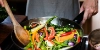 Une personne fait sauter des légumes colorés dans une poêle.