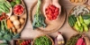 Différents légumes frais sur une table, au centre, quelqu'un tient des tomates cerises dans ses mains.