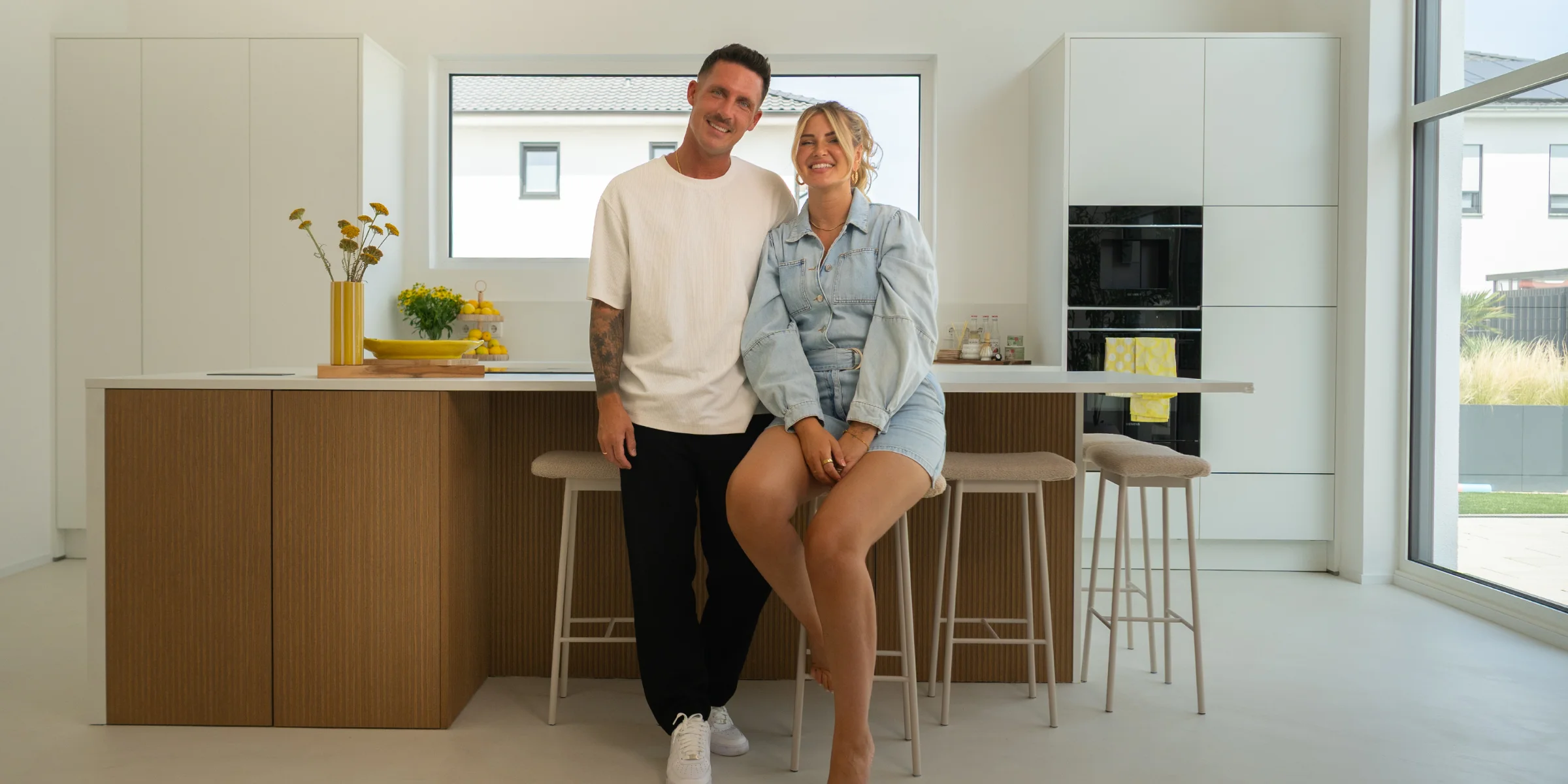 Maren et Tobias Wolf sont assis dans leur cuisine moderne Nolte avec une façade en bois clair et un grand îlot de cuisson - une combinaison harmonieuse de design et de convivialité.