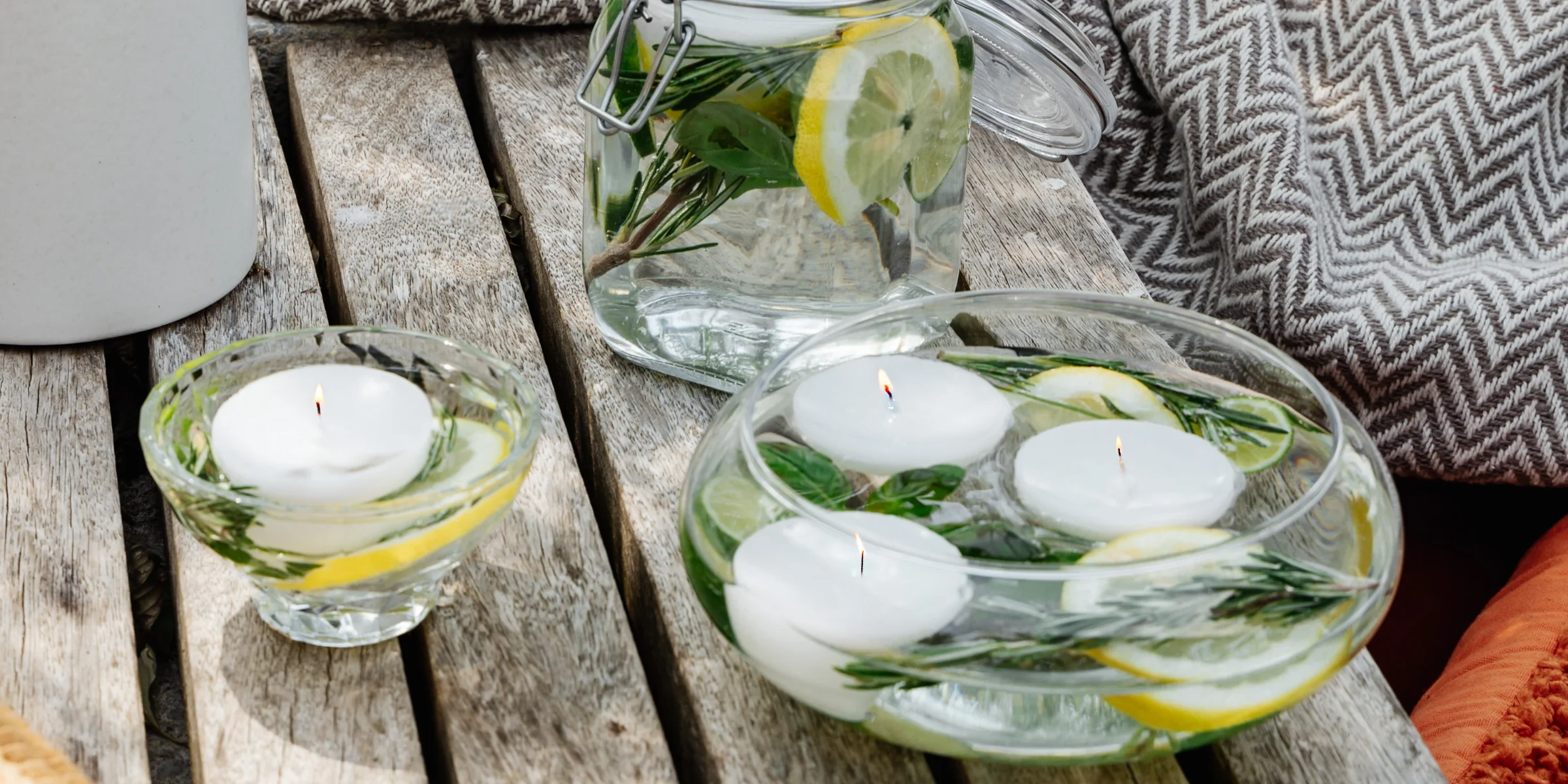 Candele al limone e alle erbe aromatiche fatte in casa, con candele galleggianti, come decorazione estiva naturale per la terrazza o il giardino.