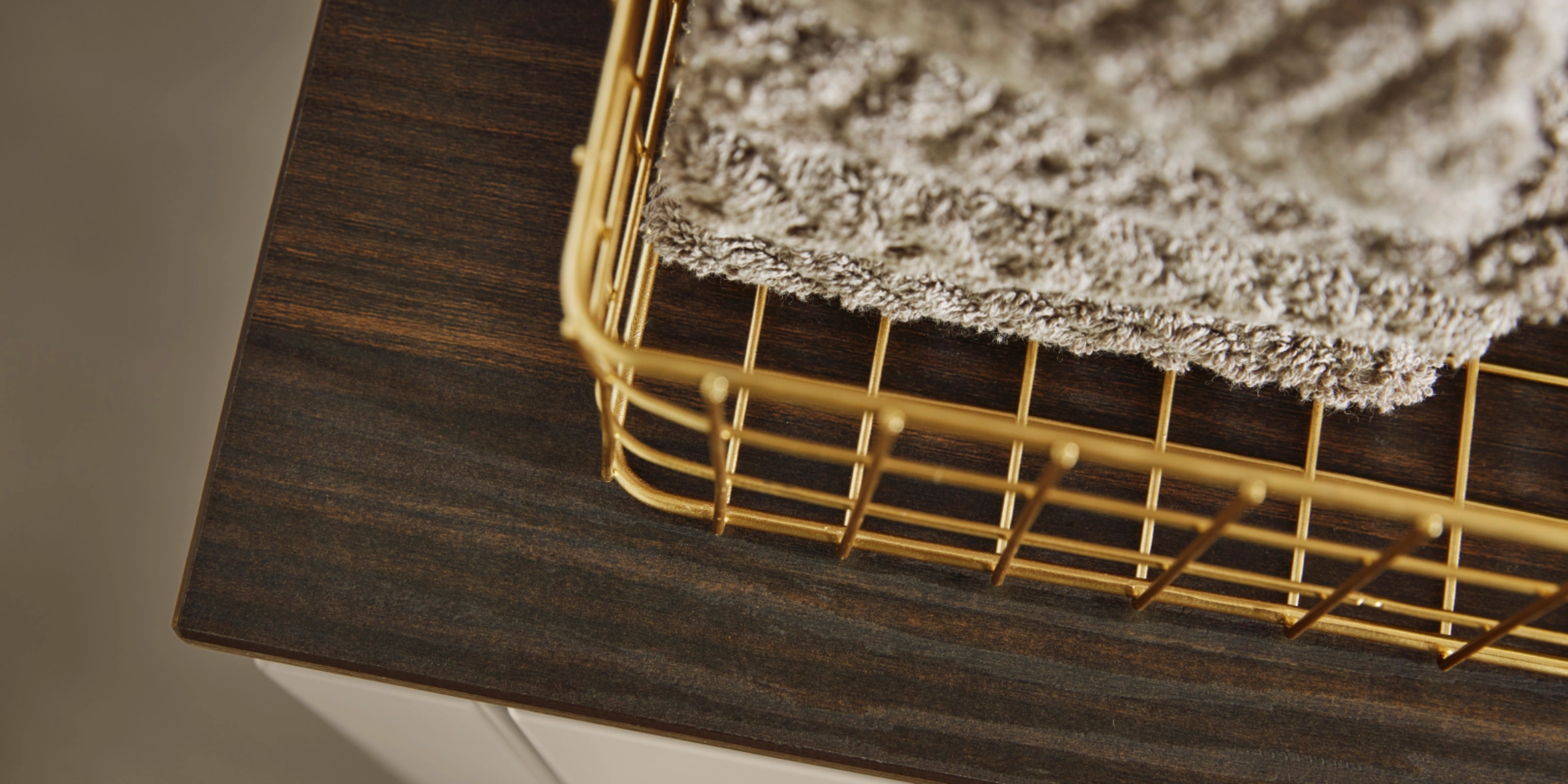 Een gouden mand met handdoeken staat op een donker houten plank van Nolte Living.