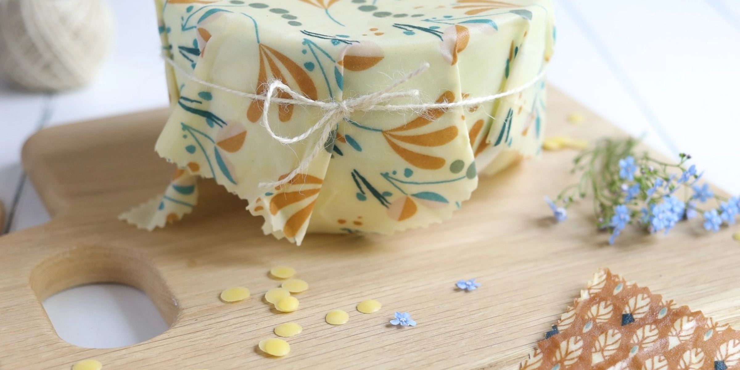 Un bol avec un tissu de cire d'abeille sur une planche en bois, entouré de fleurs et de morceaux de cire jaune.