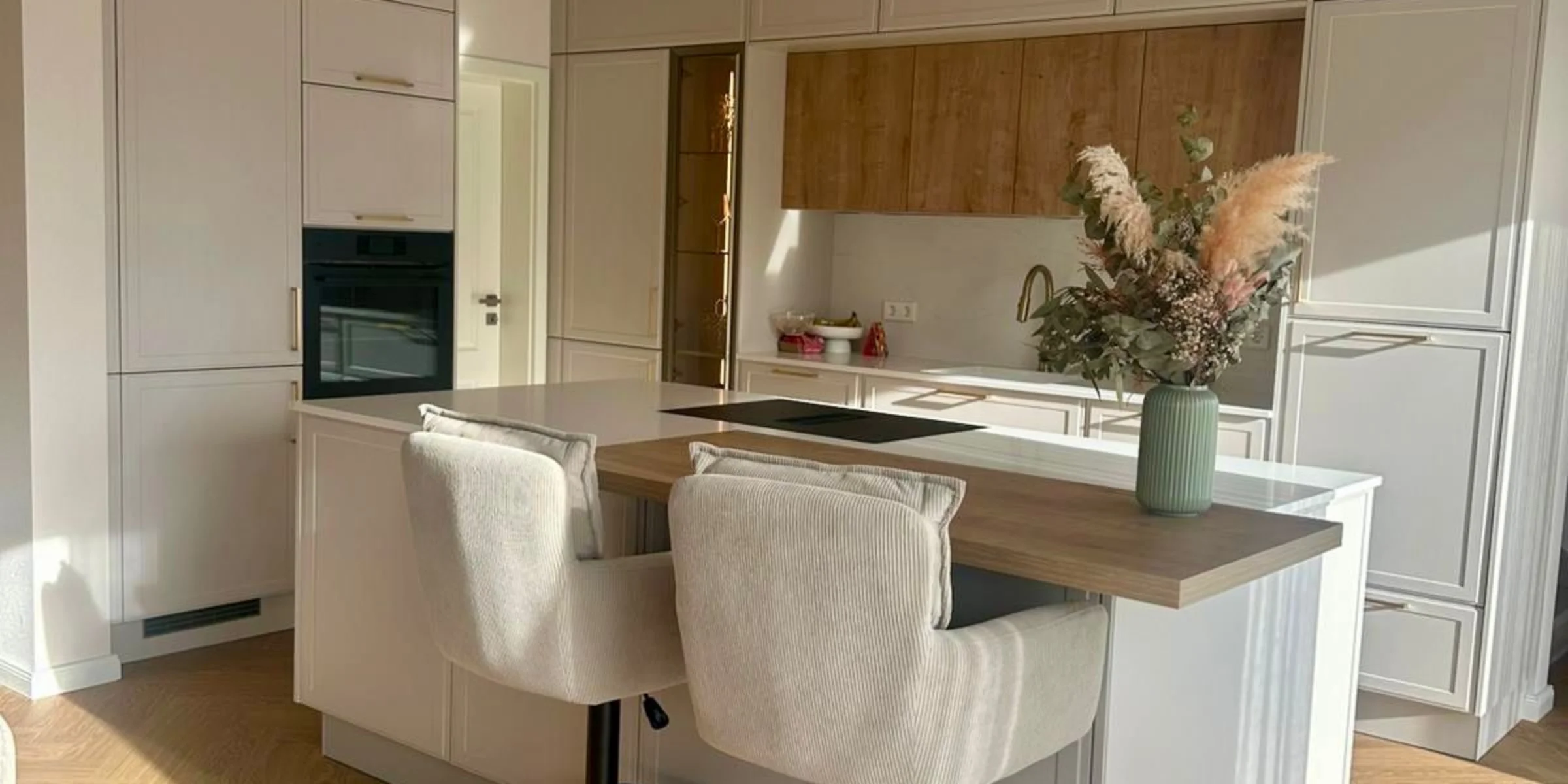 Moderne Nolte-Küche in hellem Design mit Kochinsel, Holzarbeitsplatte, Barhockern und goldenen Akzenten.