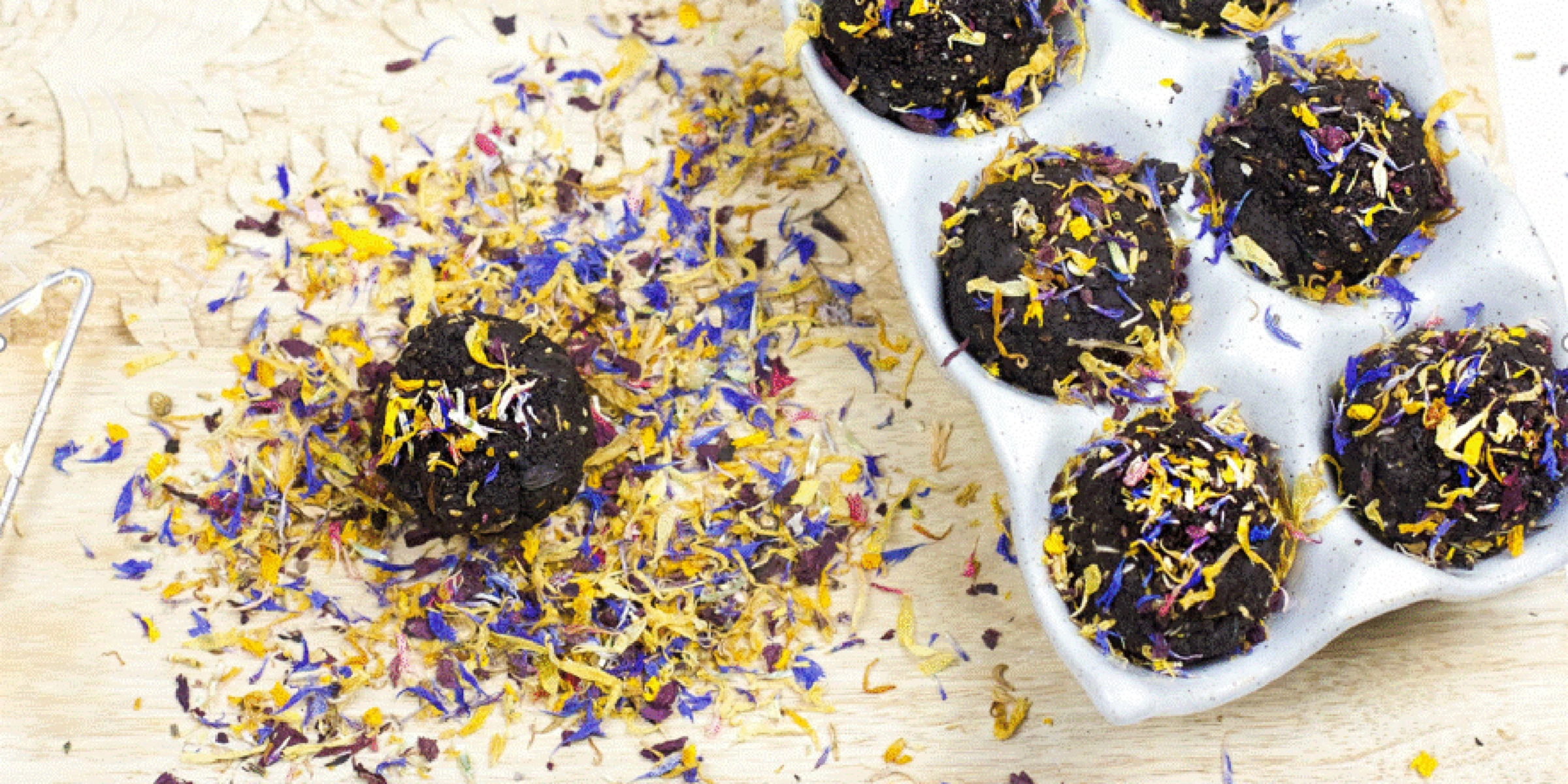 Une boîte à œufs avec des muffins au chocolat décorés de fleurs séchées sur une planche en bois.