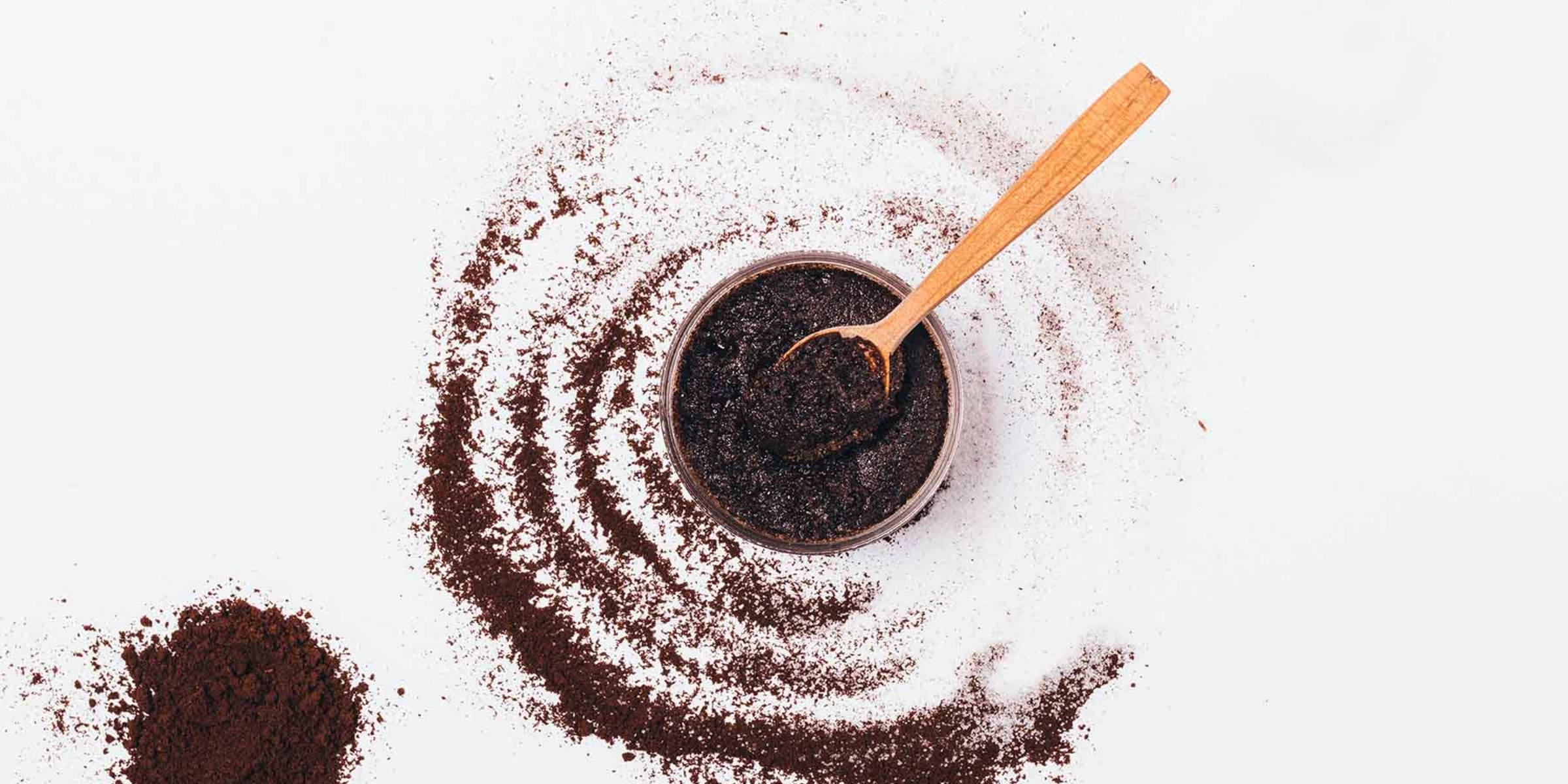 Un bol de café moulu avec une cuillère en bois, entouré de café moulu éparpillé.