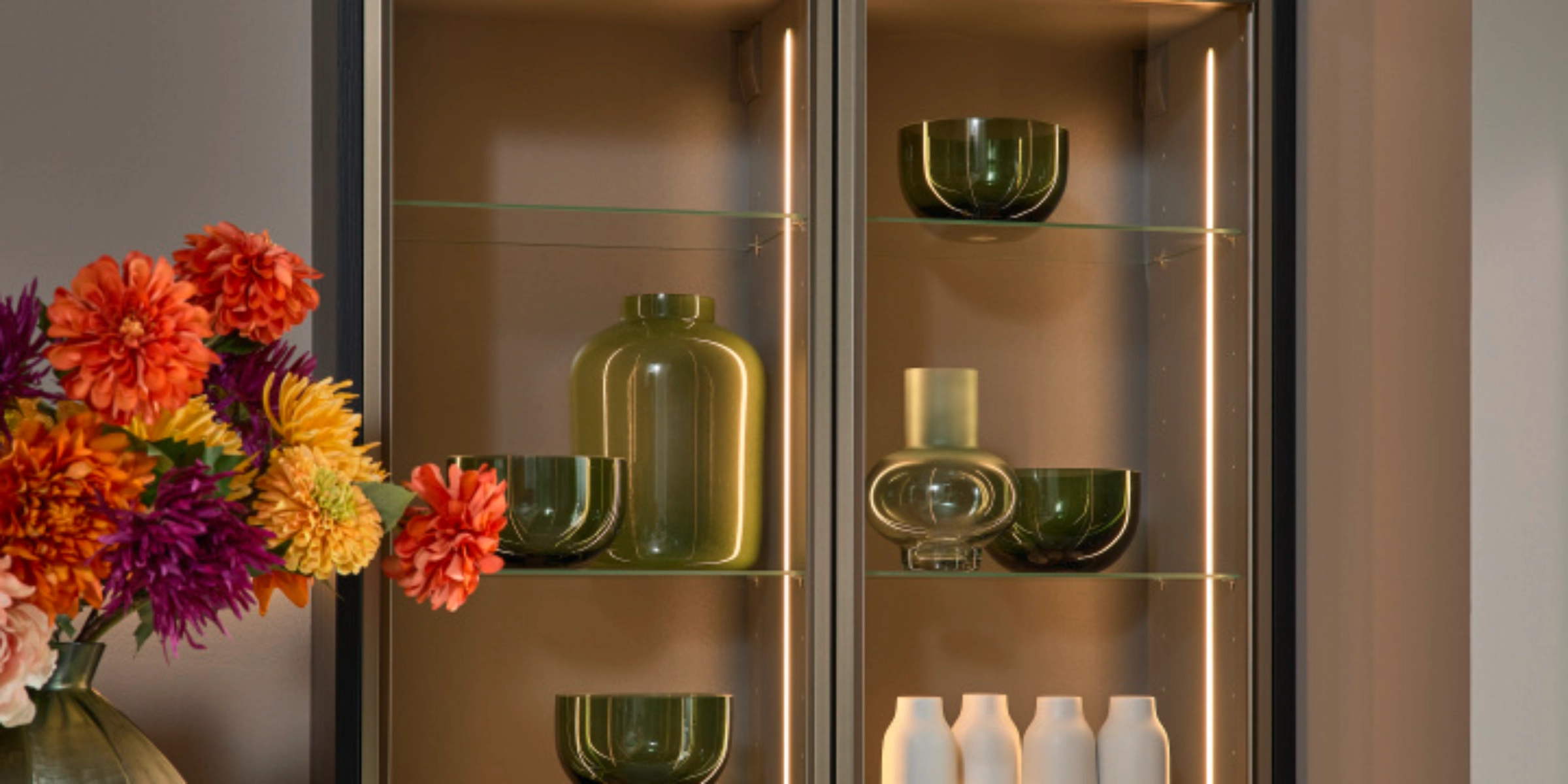 Un élégant placard de cuisine avec étagères en verre et éclairage décoratif, arrangé par Nolte Kitchen.