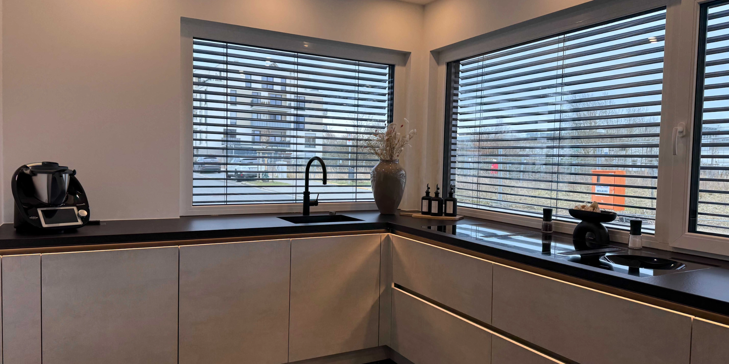 Une cuisine moderne avec grandes fenêtres et plans de travail sombres. Nolte Kitchen.