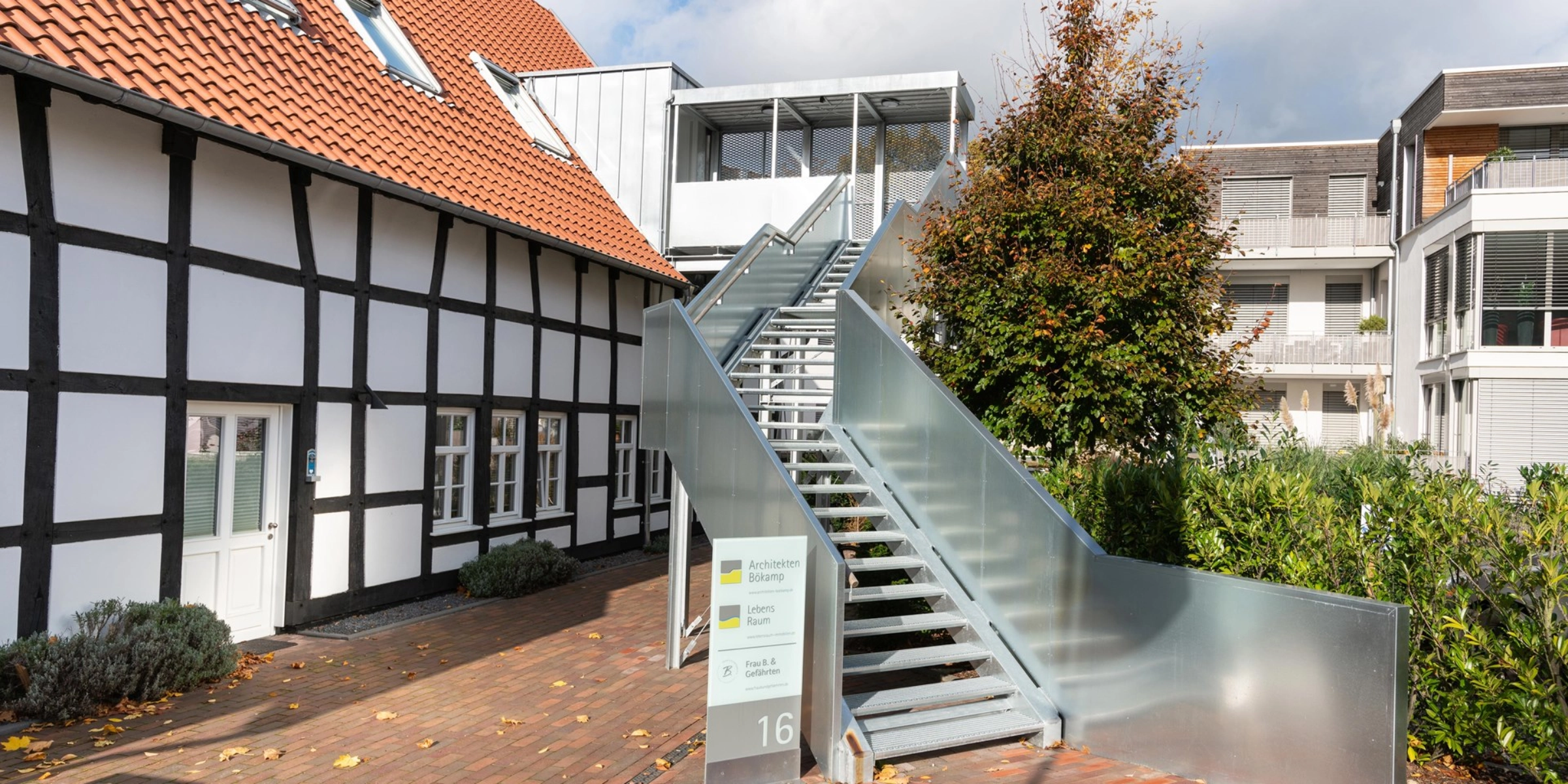 Un bâtiment moderne avec escalier extérieur à côté d'une maison à colombages sous un ciel nuageux.