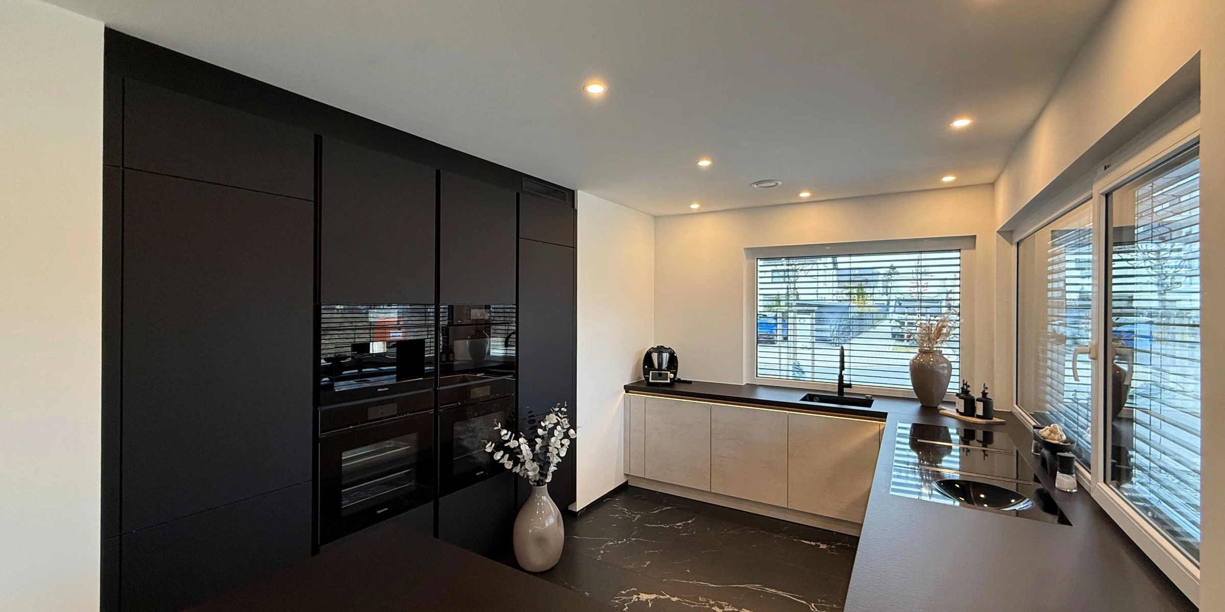 Cuisine moderne avec armoires sombres et îlot central de cuisson par Nolte Kitchen.