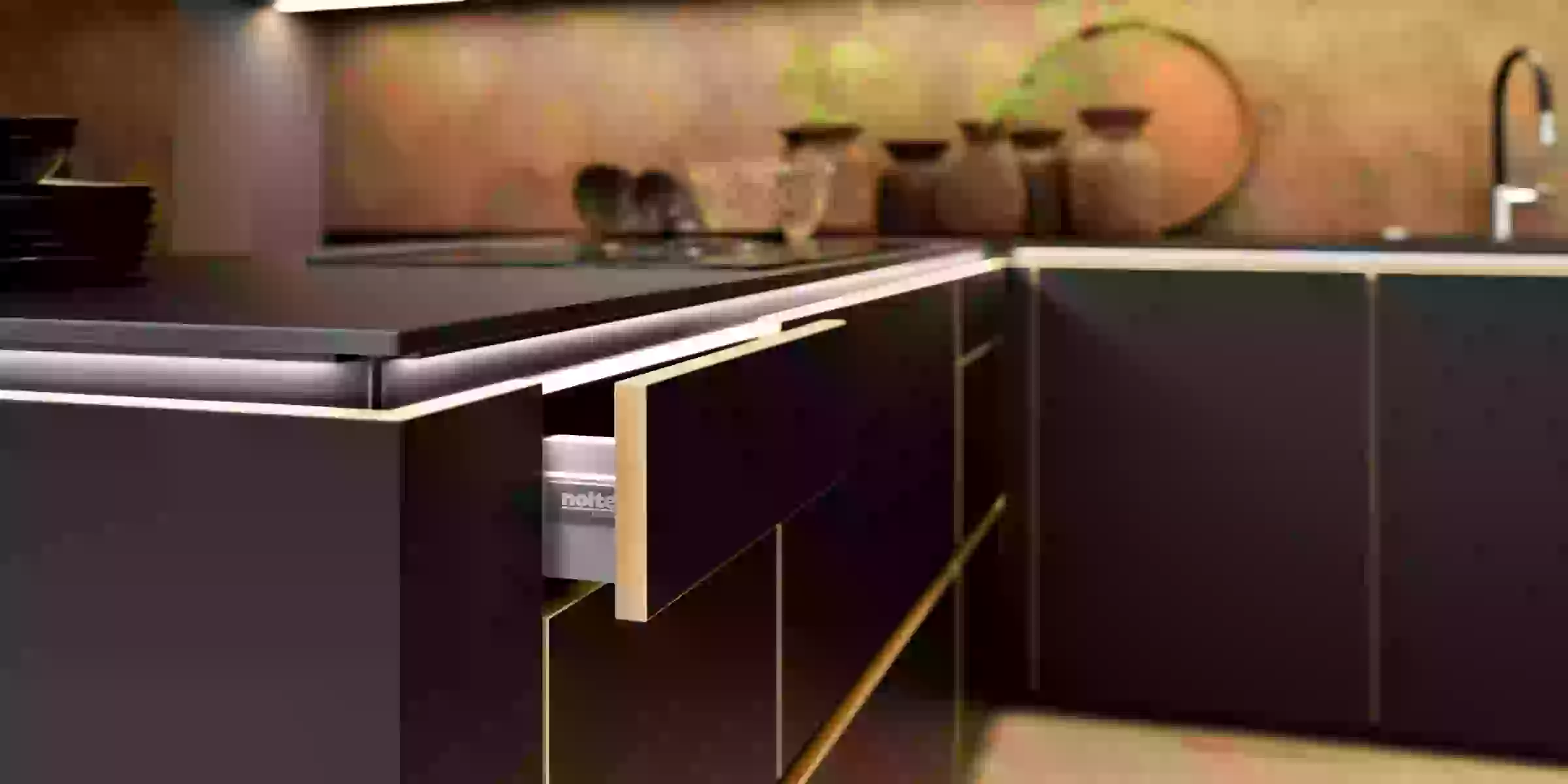 Cuisine moderne avec armoires noires et accents dorés, conçue par Nolte Kitchen.