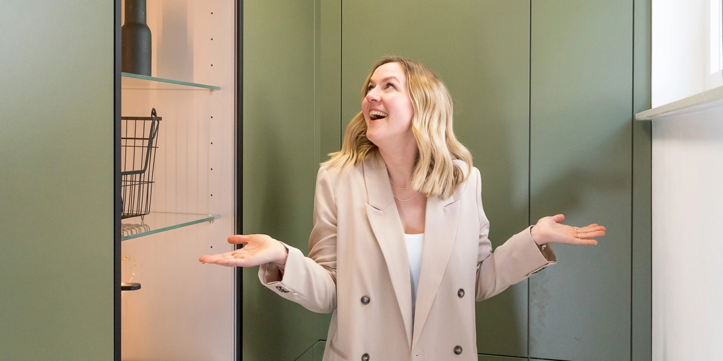 Une femme se tient dans une buanderie moderne avec des armoires vertes de Nolte Utility Rooms.