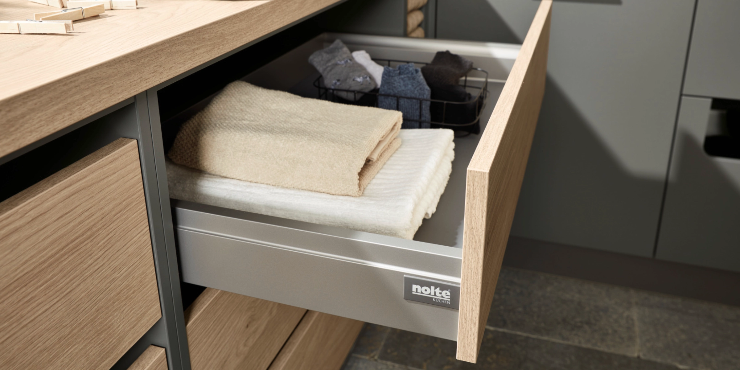 Un meuble à tiroirs ouvert avec des serviettes et des vêtements dans une buanderie de Nolte Utility Rooms.
