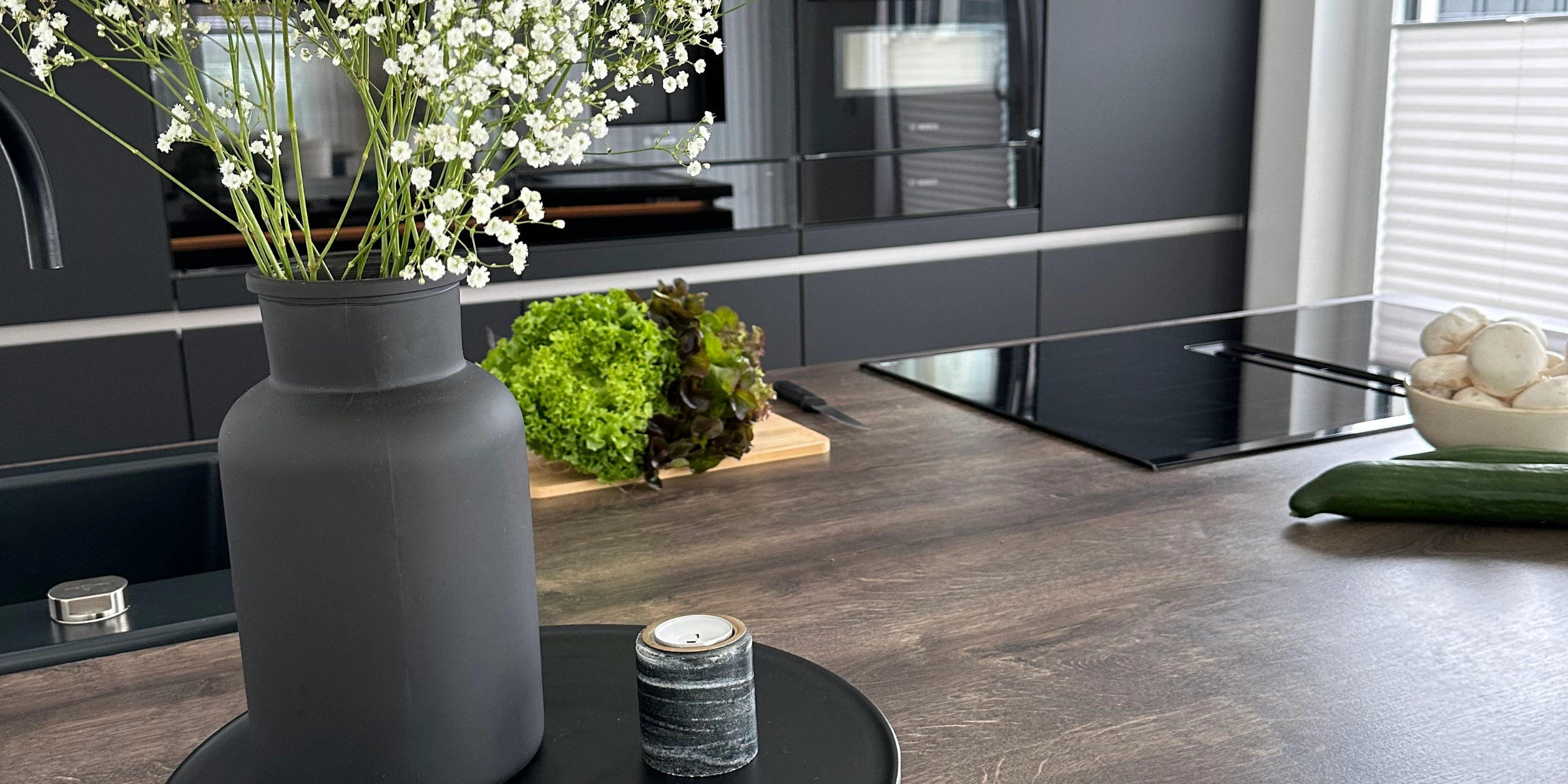 A vase with flowers sits on the countertop in a modern kitchen with dark cabinets. Nolte Kitchens.