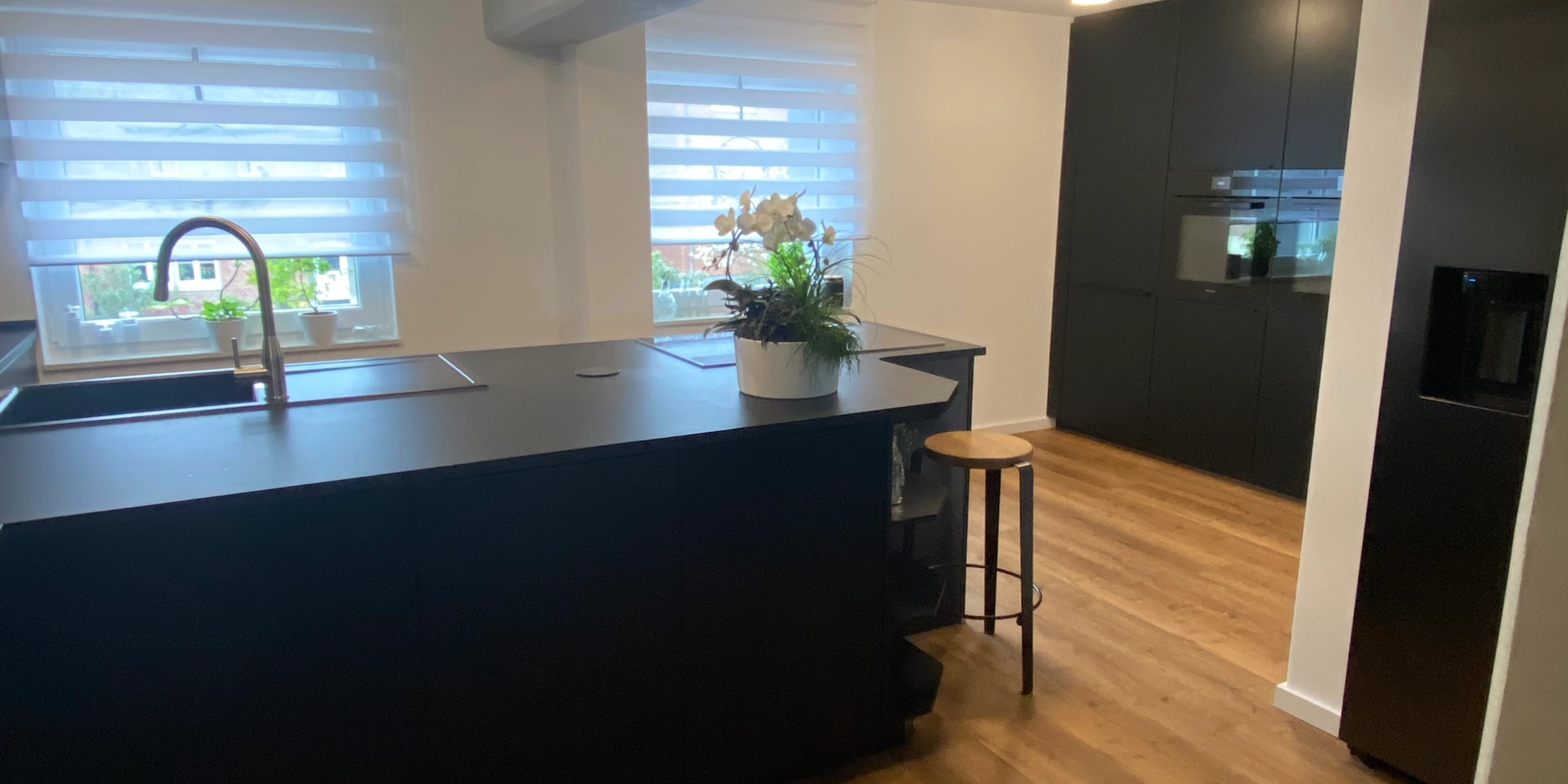 Cuisine moderne avec armoires sombres et sol en bois, équipée par Nolte Kitchen.
