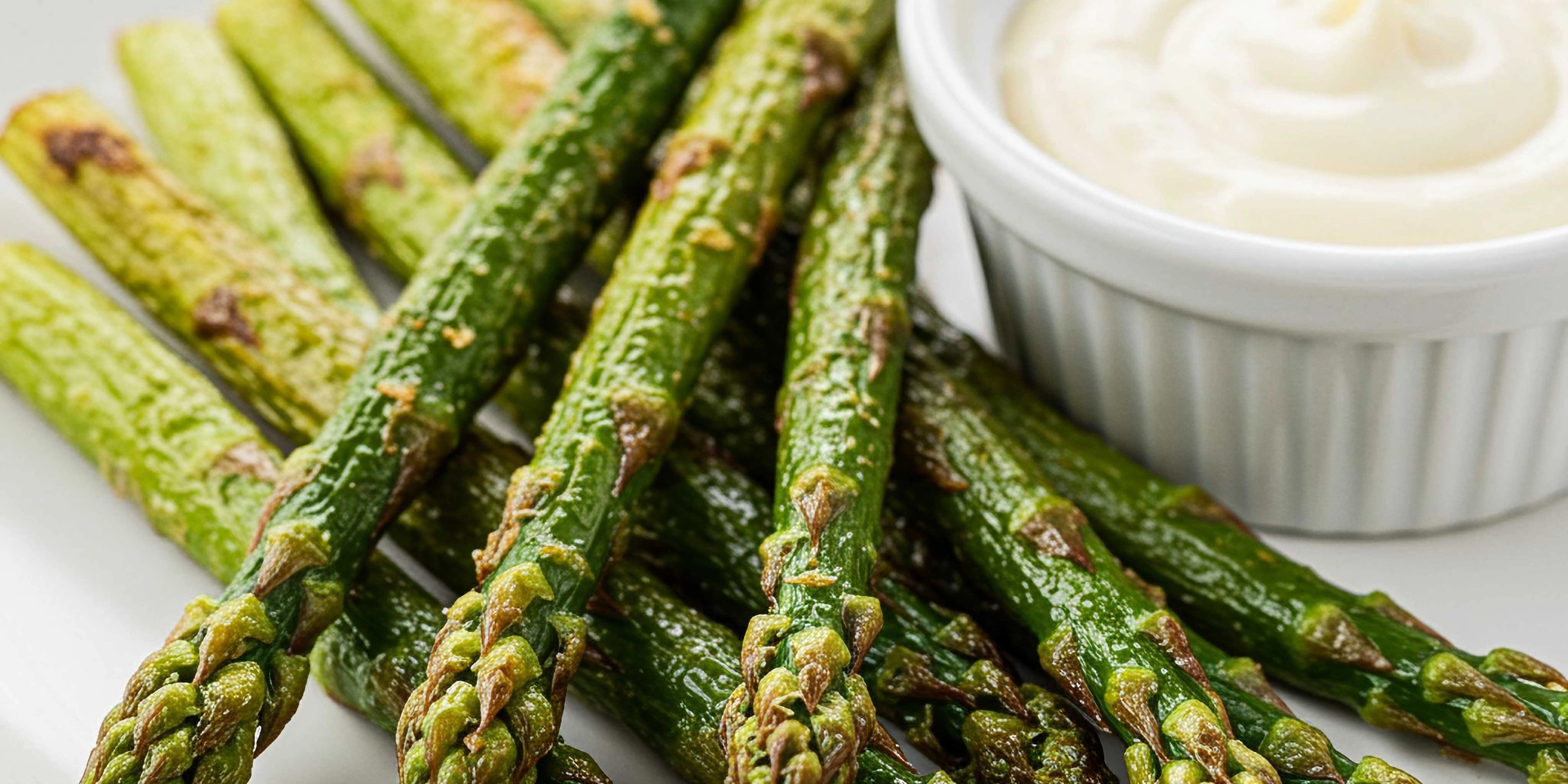 Green asparagus on a white plate with a bowl of dip.