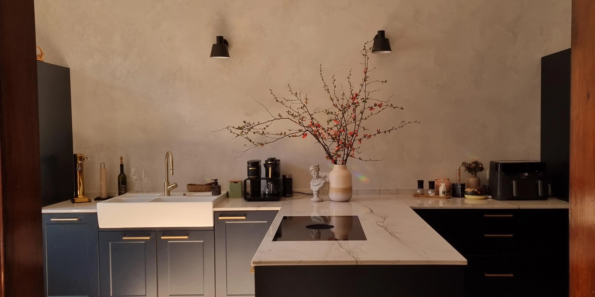 Cuisine moderne avec îlot et armoires sombres, éclairée par un lustre. Nolte Kitchen.