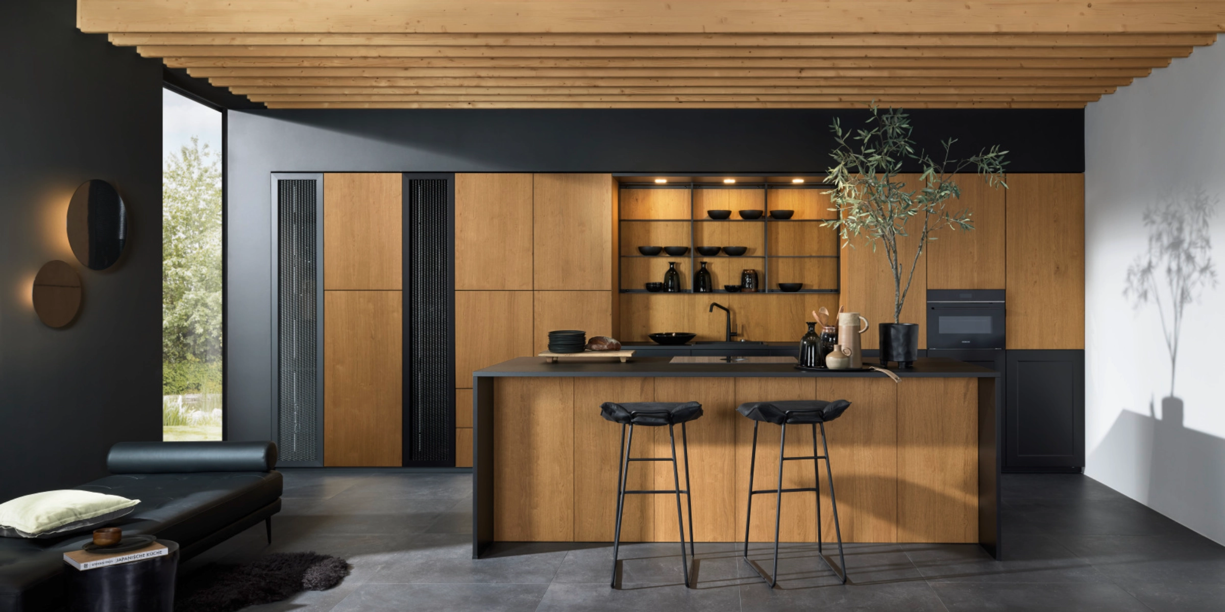 Cuisine Nolte moderne avec la façade exclusive en bois véritable neoNATURE en chêne Cottage. L’aspect chaleureux du bois est élégamment complété par des accents noirs et des étagères ouvertes. L’îlot de cuisine avec espace assis et le concept d’éclairage bien pensé créent une ambiance conviviale avec une élégance naturelle.