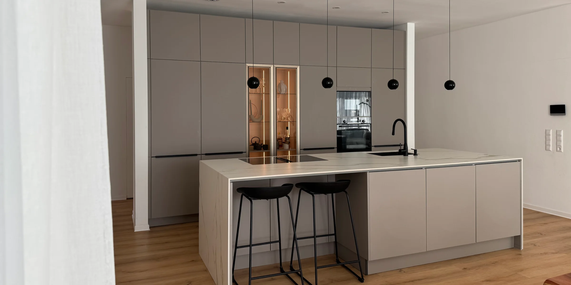 Moderne Nolte Küche mit Kücheninsel in Marmoroptik und beleuchteter Bronze-Vitrine.