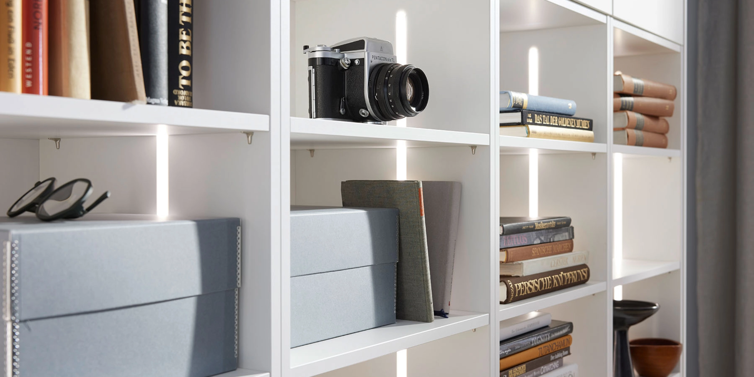 Une étagère avec des livres, un appareil photo et des boîtes; exemple de rangement élégant par Nolte Living.