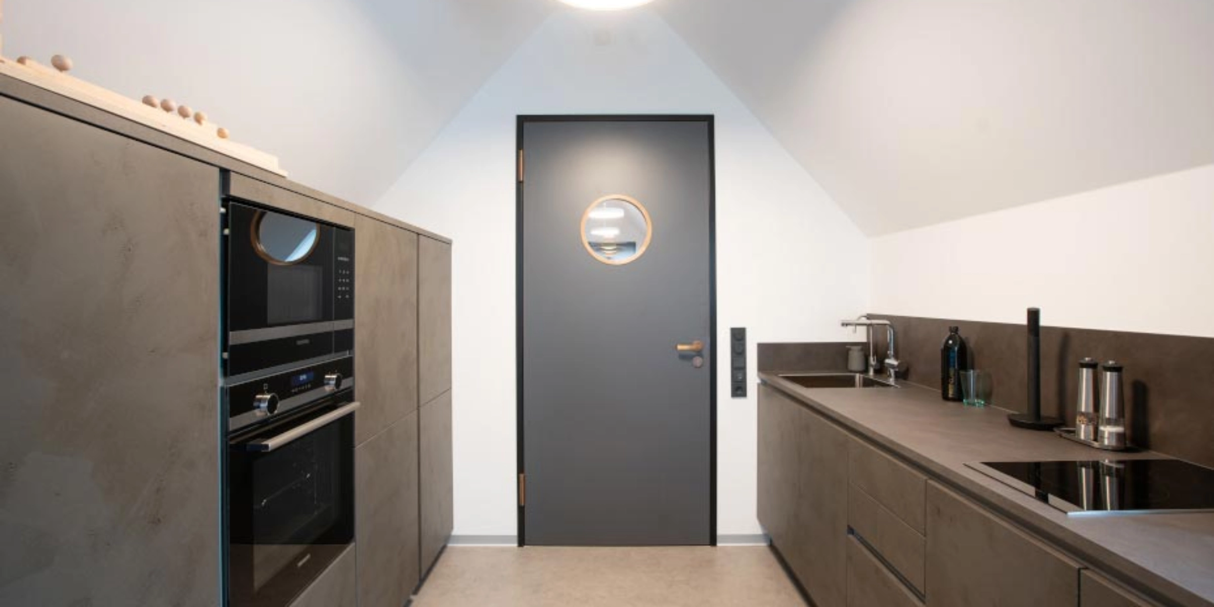 Cuisine moderne avec armoires grises et appareils sous un toit en pente, Nolte Kitchen.