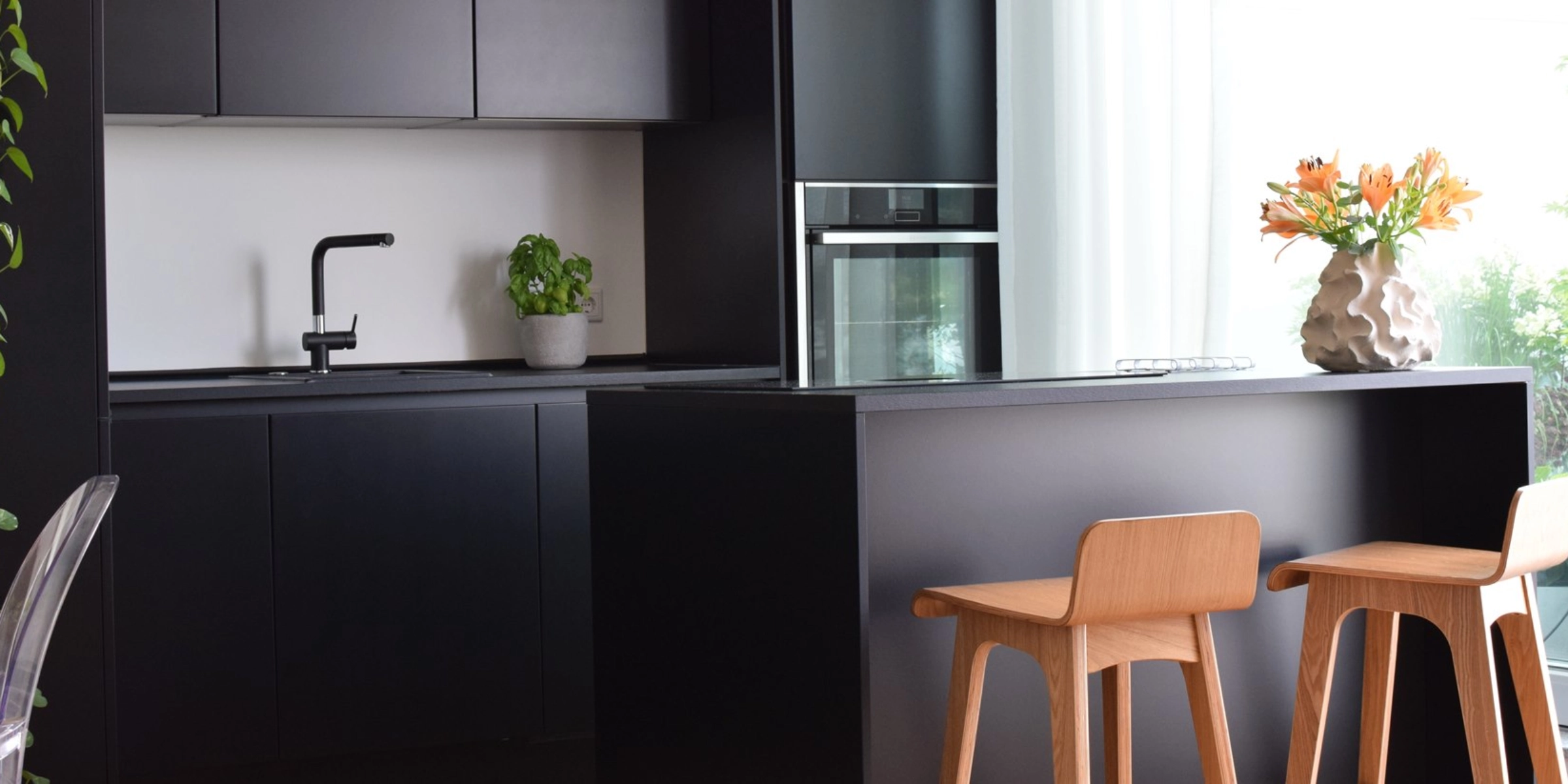 Cuisine moderne noire avec îlot et chaises en bois, décorée de plantes. Nolte Kitchen.