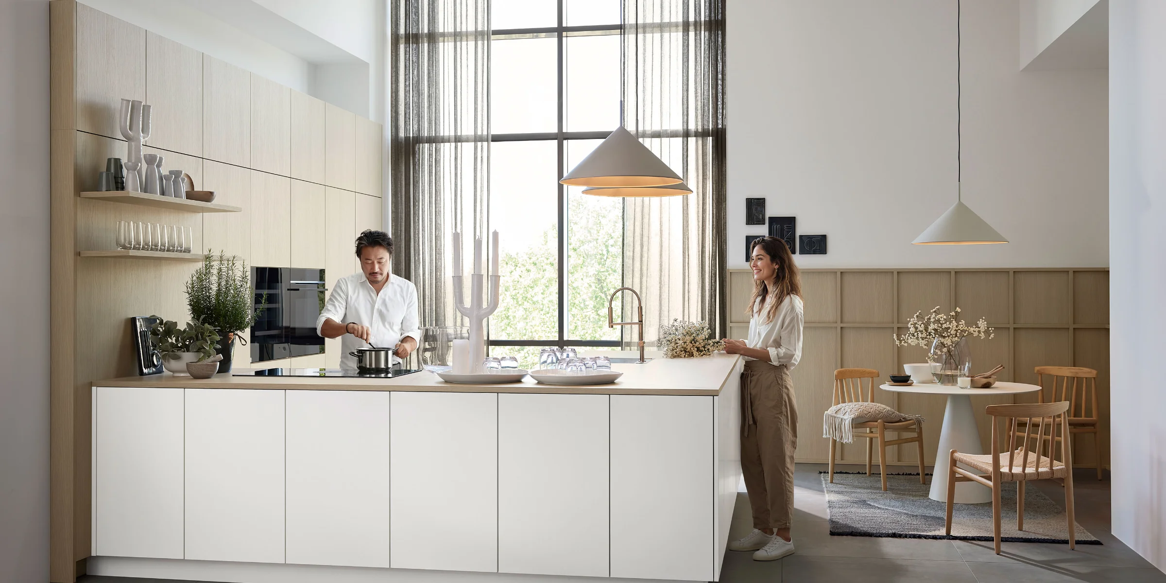 Moderne Nolte Küche mit Kochinsel: Person kocht am Herd, während eine zweite Person daneben steht – großzügige Arbeitsbereiche und offene Raumgestaltung.