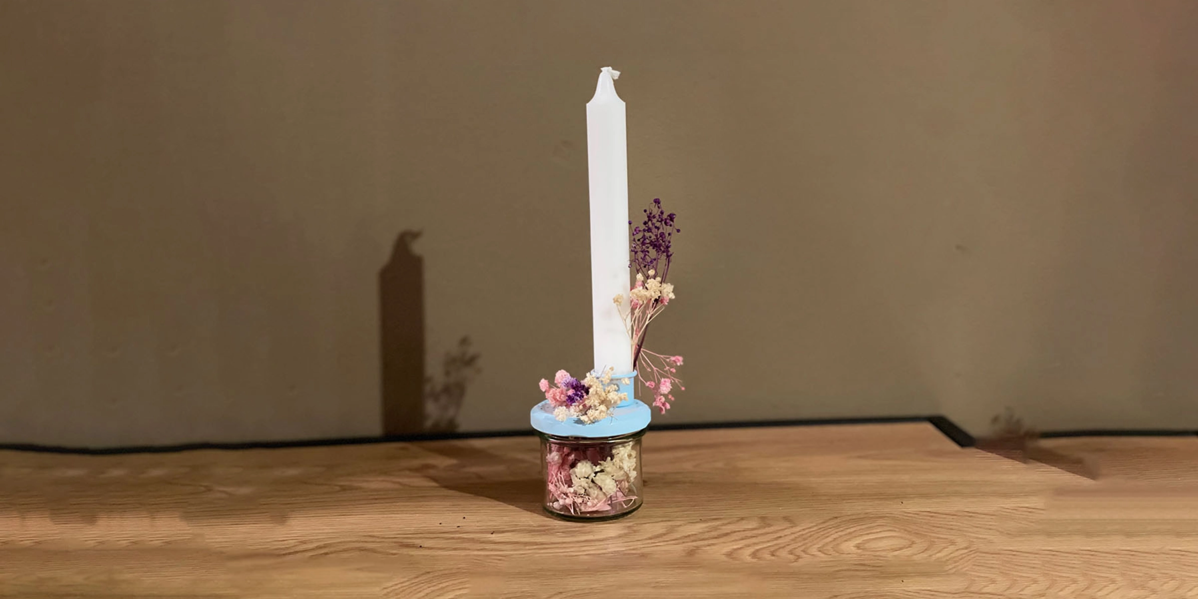 Une bougie allumée sur une table en bois, décorée de fleurs séchées.