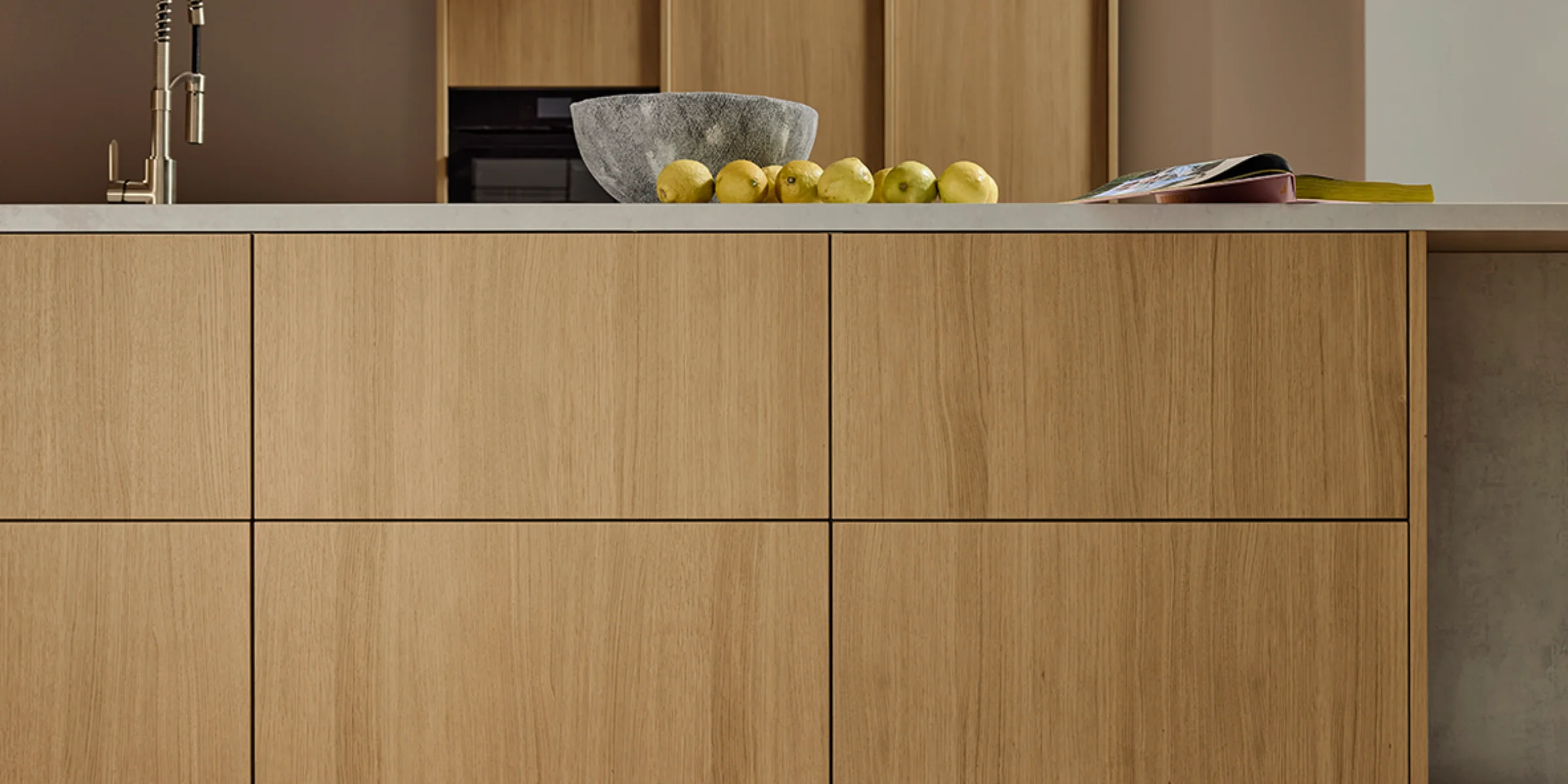 Nowoczesna kuchnia z frontami drewnianymi i jasnym blatem, udekorowana misą i owocami