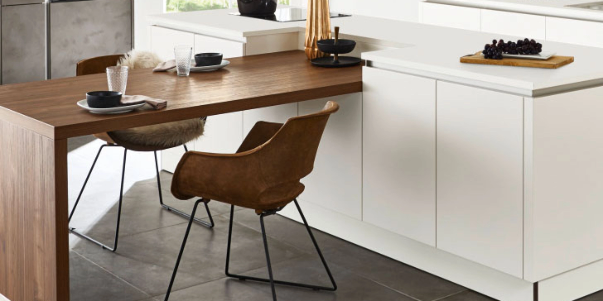 Moderne keuken met houten eettafel, witte kasten, gedecoreerd met servies en bloemen. Nolte Keukens.