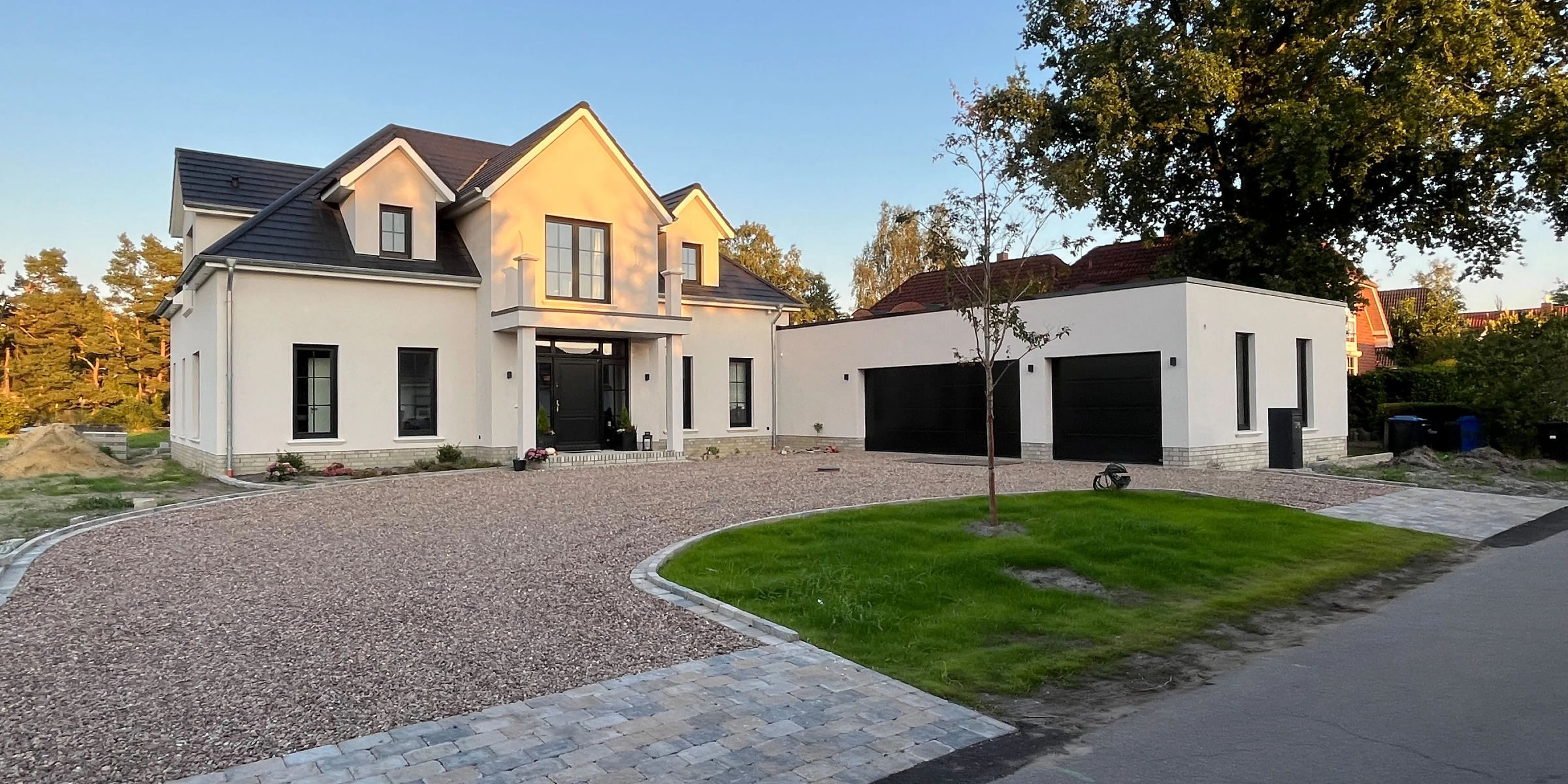 Maison moderne avec grand jardin et allée pavée au coucher du soleil.