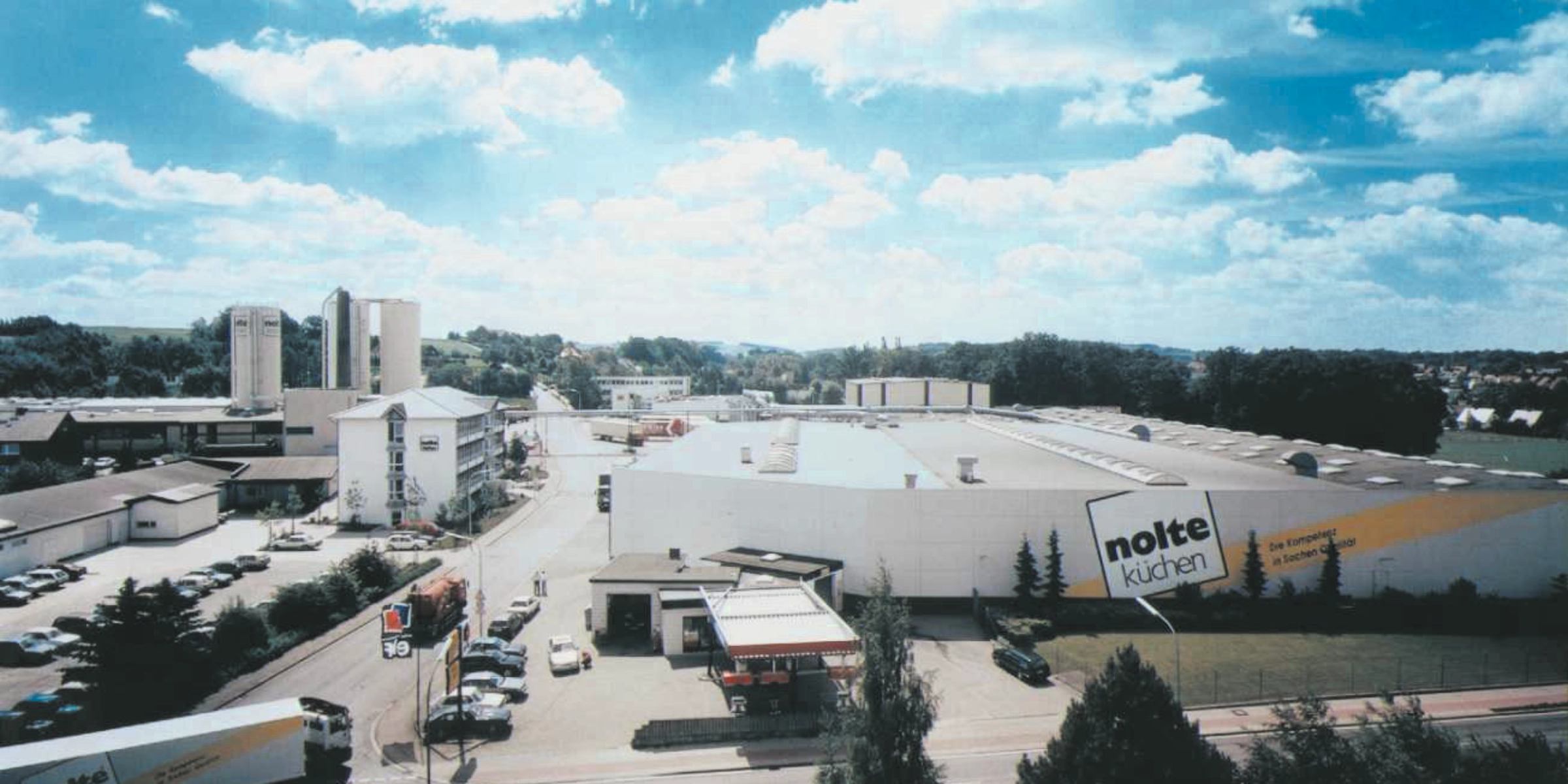 Grande usine avec l'inscription "nolte küchen" sur le toit sous un ciel nuageux.