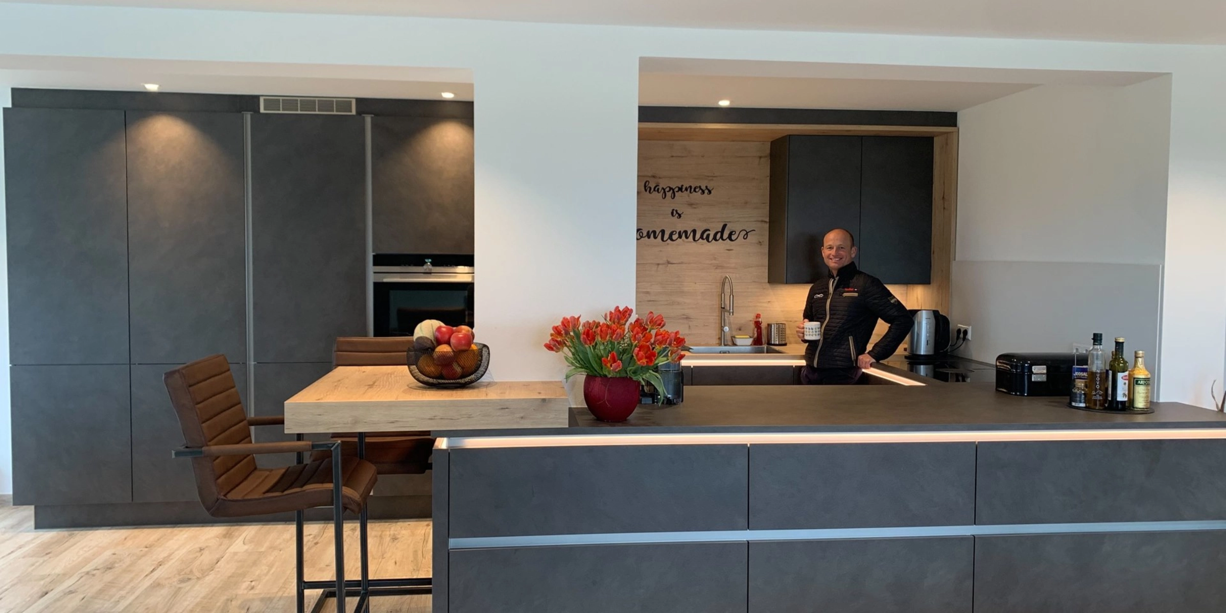 Cucina moderna con armadi scuri e una persona al bancone. Nolte Kitchen.