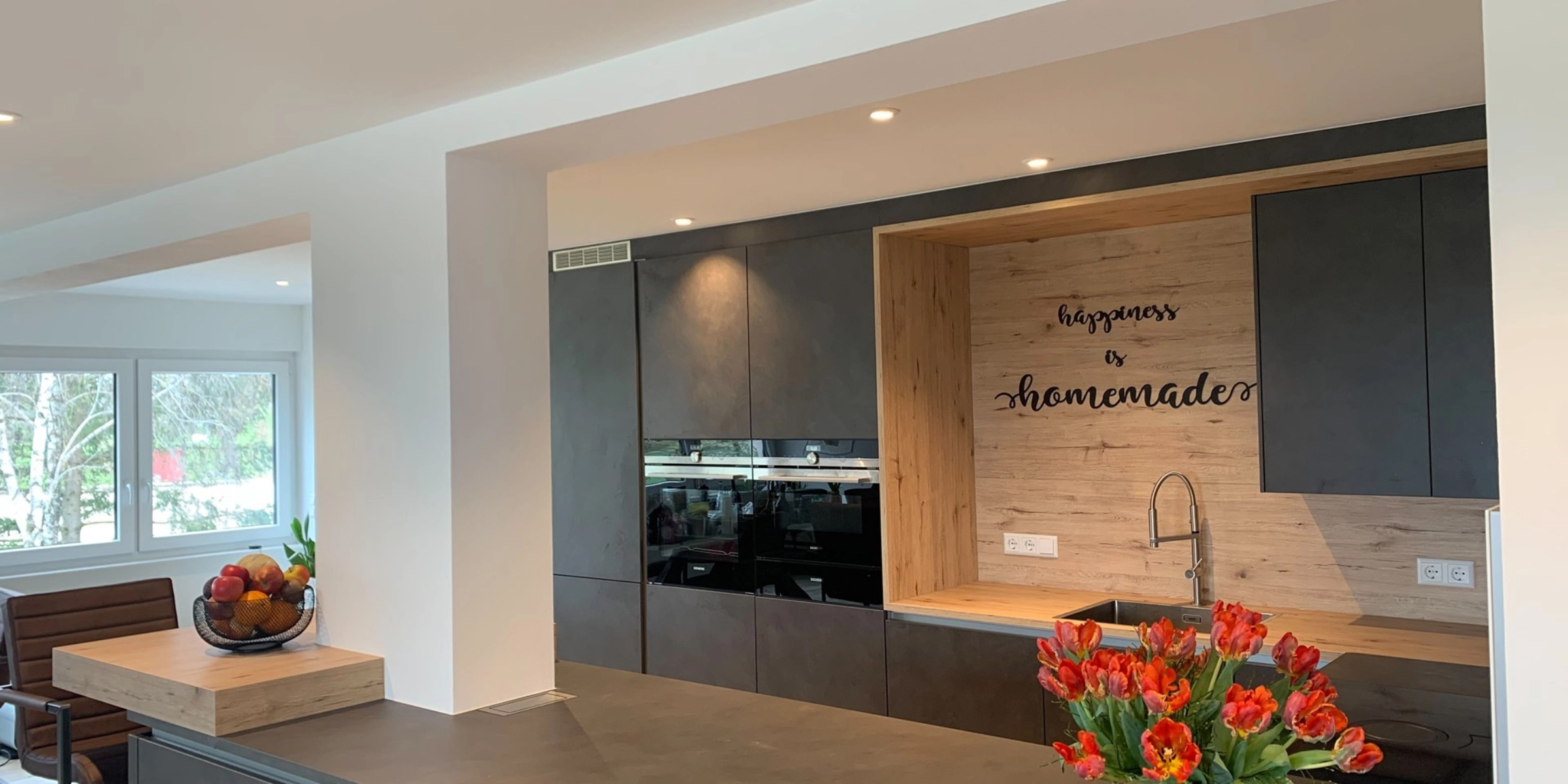 Cucina moderna con armadi scuri e tulipani sul bancone, design di Nolte Kitchen.