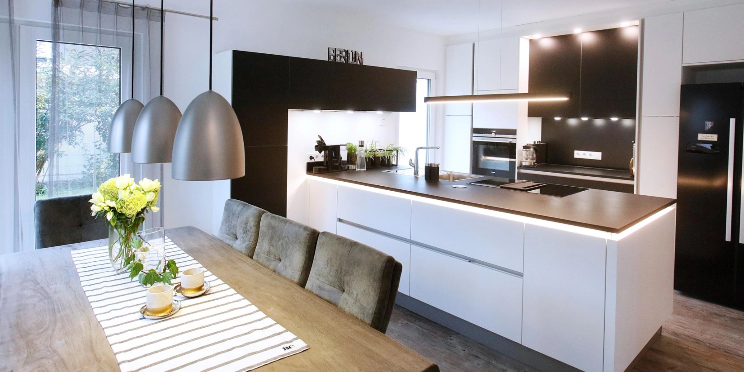 Cucina moderna con tavolo da pranzo e lampade a sospensione, presentata da Nolte Kitchen.
