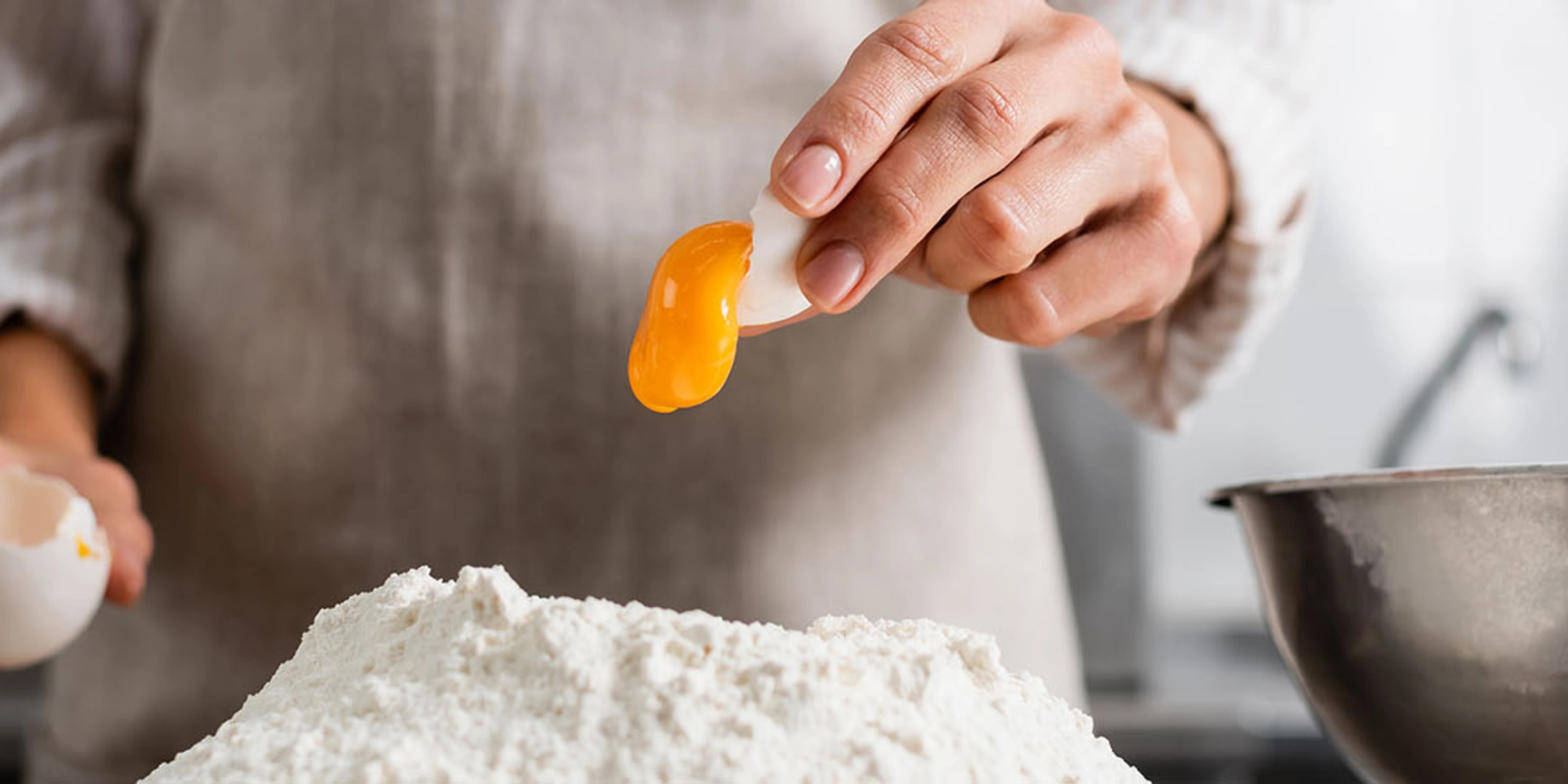 Une personne sépare un jaune d'œuf au-dessus d'un tas de farine dans une cuisine moderne de Nolte Kitchen.