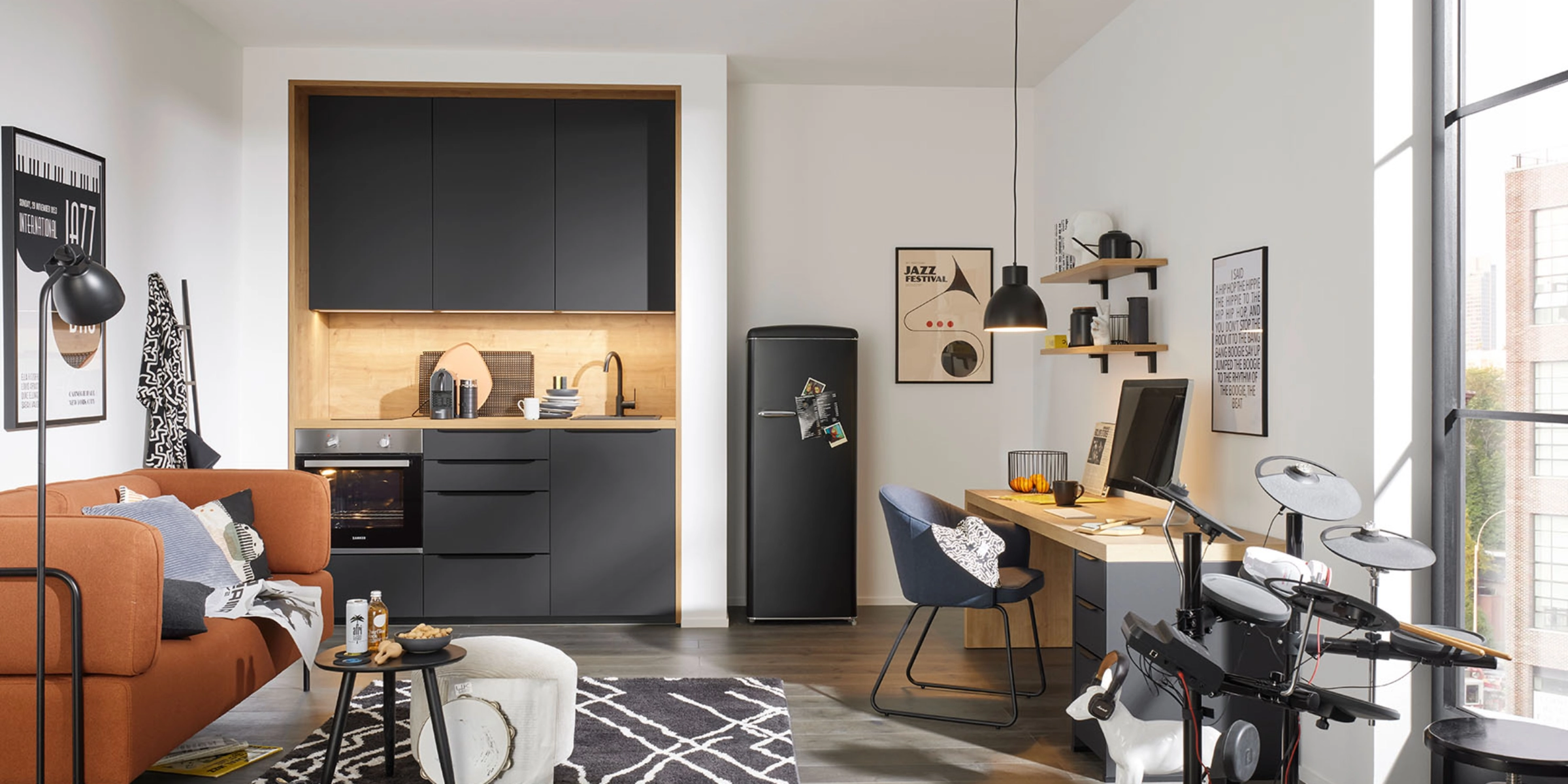 Dans une pièce moderne avec une cuisine grise Nolte, on voit un canapé, un bureau et une batterie électronique.