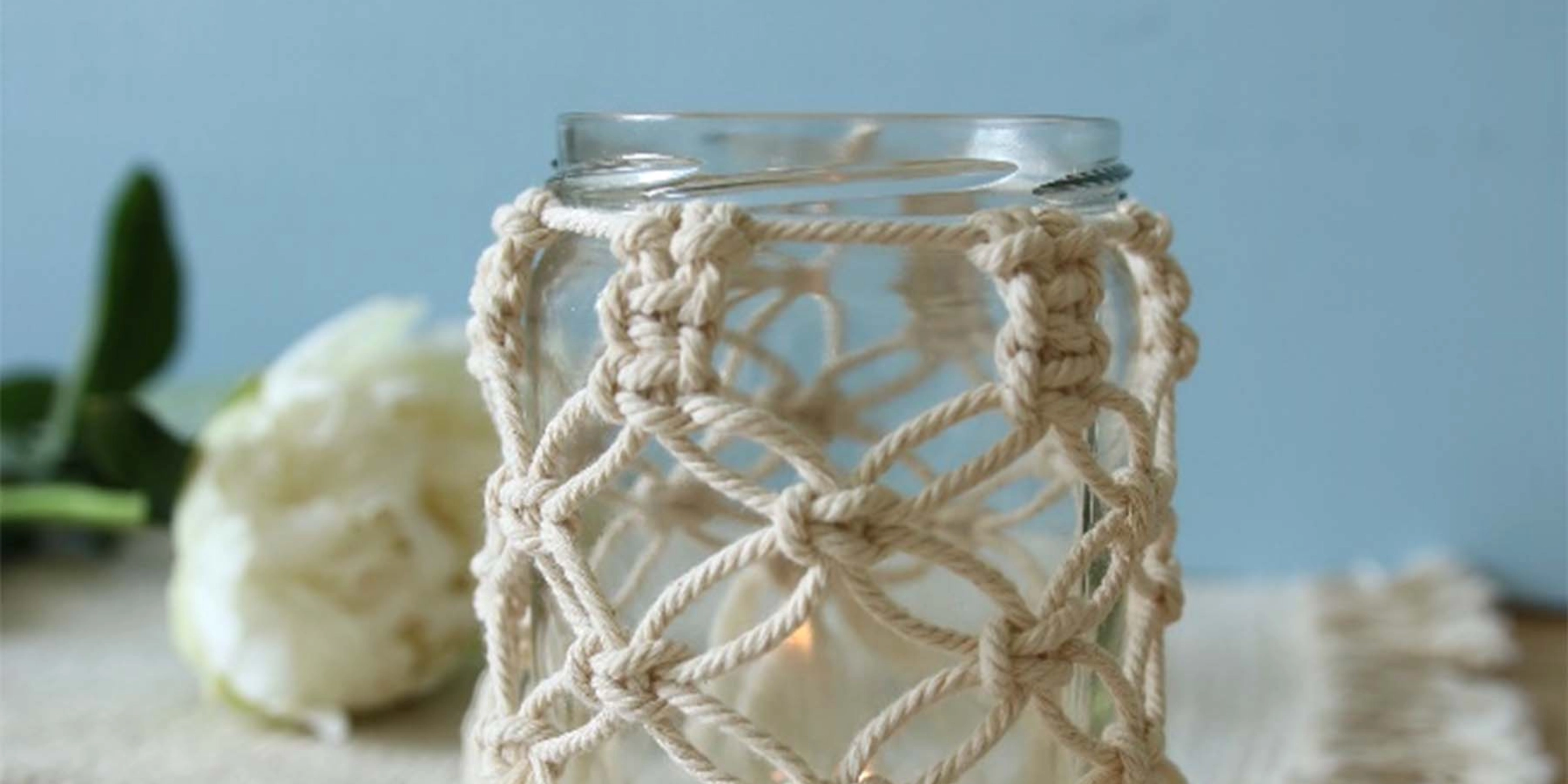 Un verre avec une housse en macramé sur une table avec une nappe à franges.
